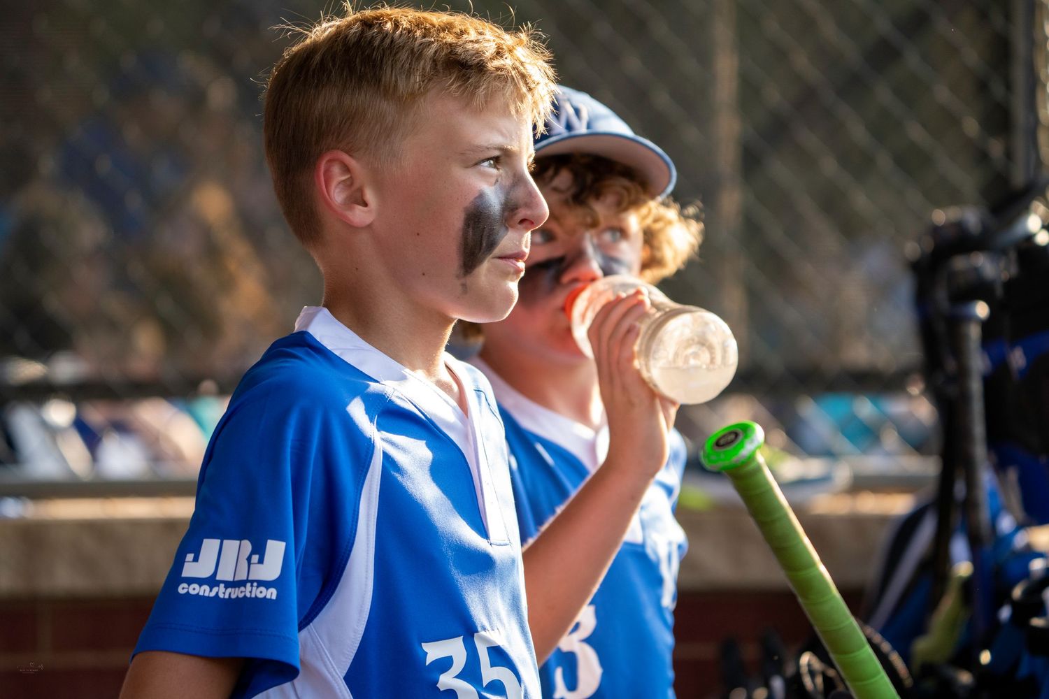 Young baseball players in blue jerseys take a break to enjoy drinks during a game break at the field.