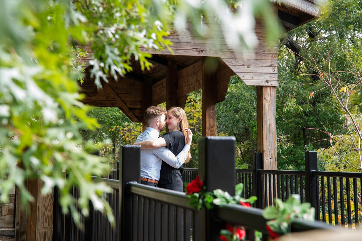 A couple shares a romantic moment on a rustic wooden deck surrounded by lush greenery and trees.