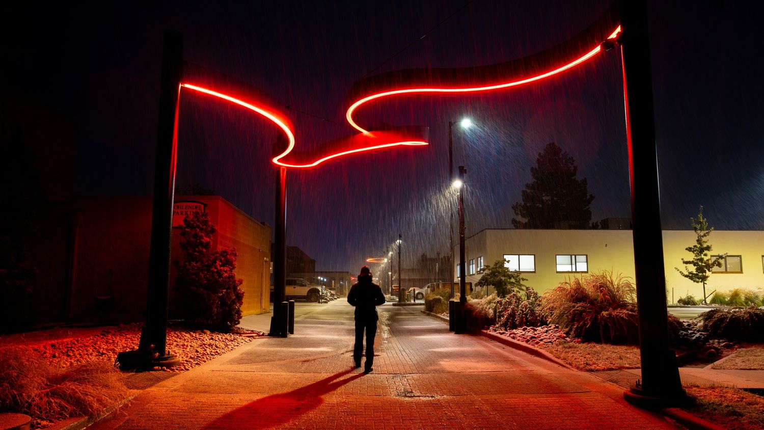 Silhouetted figure walking under glowing red neon arch installation at night.