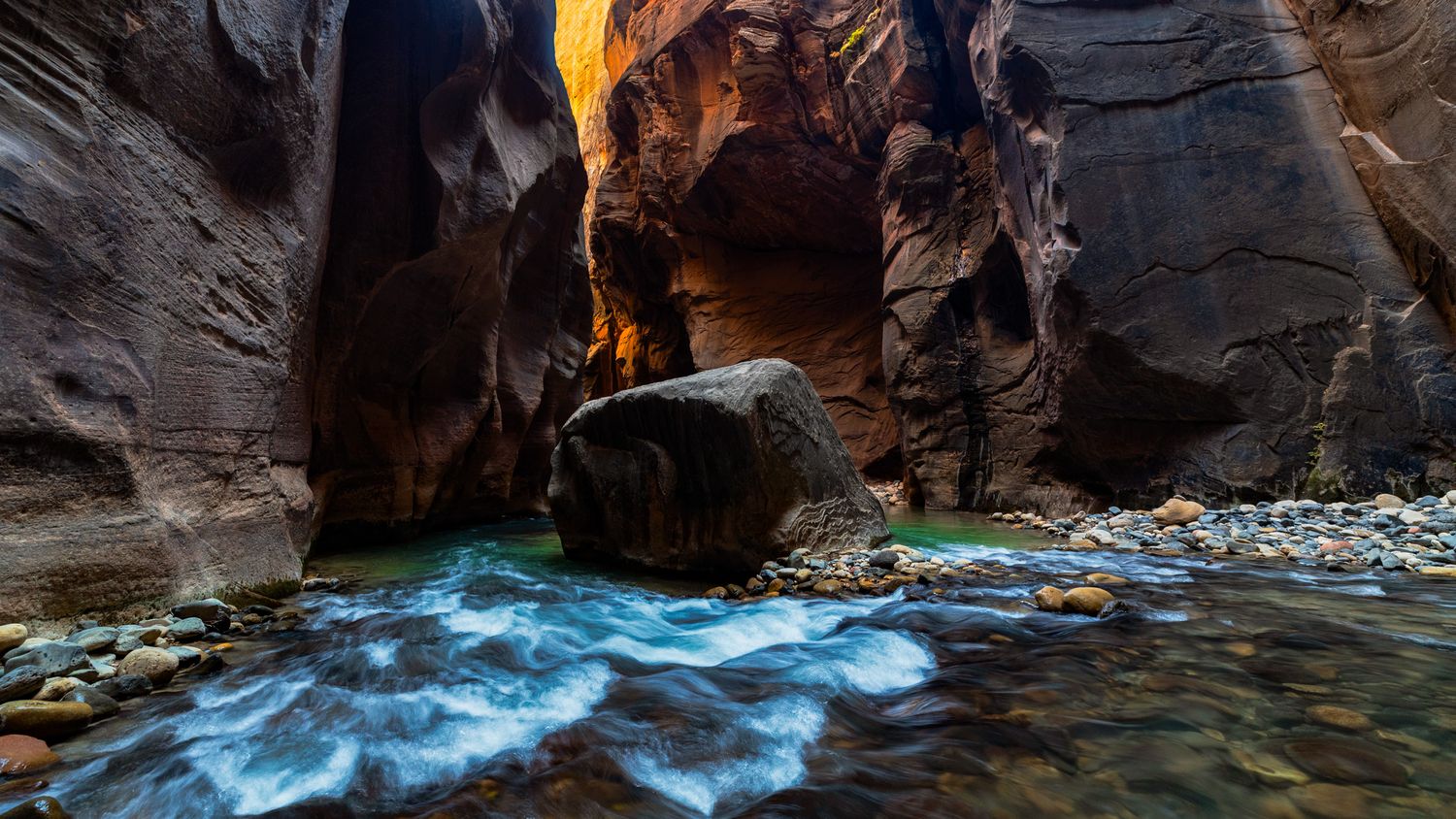 Narrow slot canyon with glowing orange walls carved by flowing water. Zion National Park. The Narrows