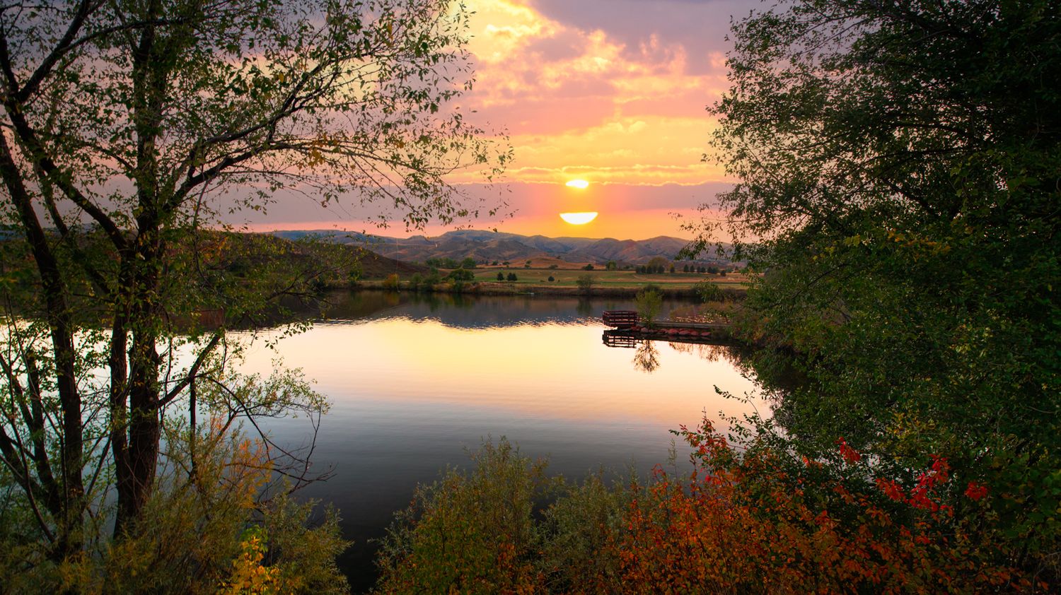 Panoramic autumn landscape with colorful trees silhouetted against dramatic sunset sky.