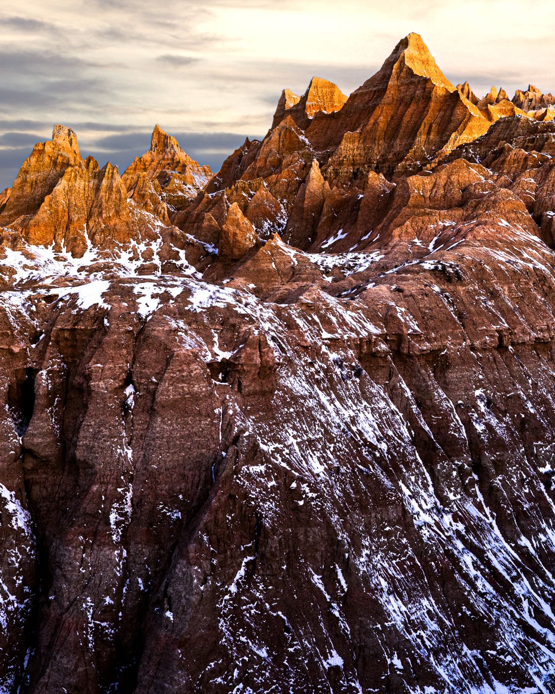 Jagged mountain peaks dusted with snow glow orange in the sunset light. Badlands National Park
