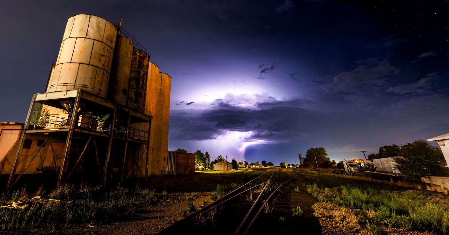 Industrial storage tank against dramatic lightning storm sky at night.