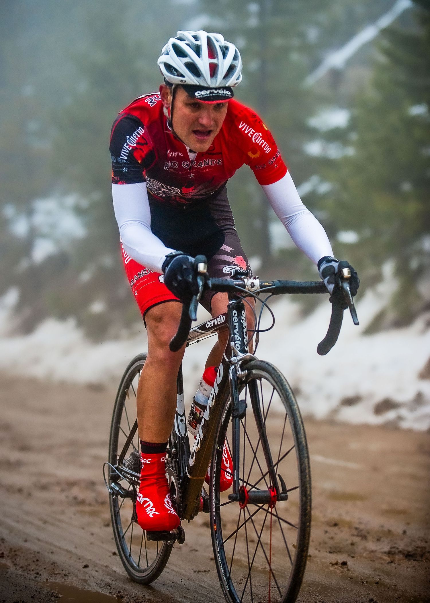 Cyclist in red and white racing gear navigates a dirt trail on a professional racing bike.