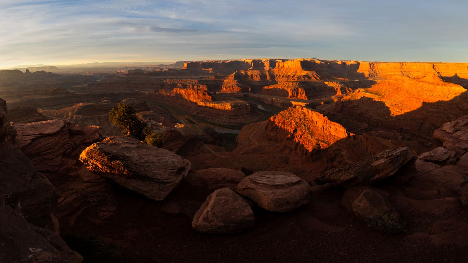 Dramatic panorama of canyon walls glowing orange during sunset with layered rock formations.