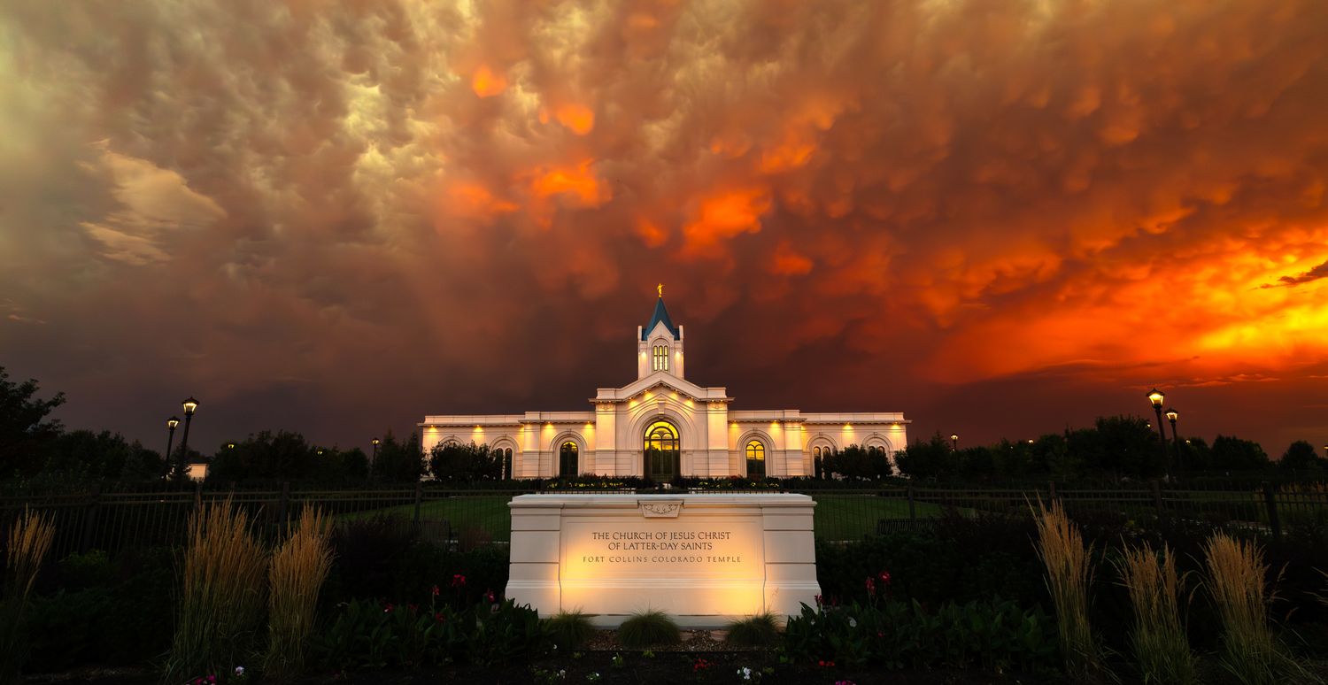 Mormon temple building illuminated at sunset with dramatic orange storm clouds.