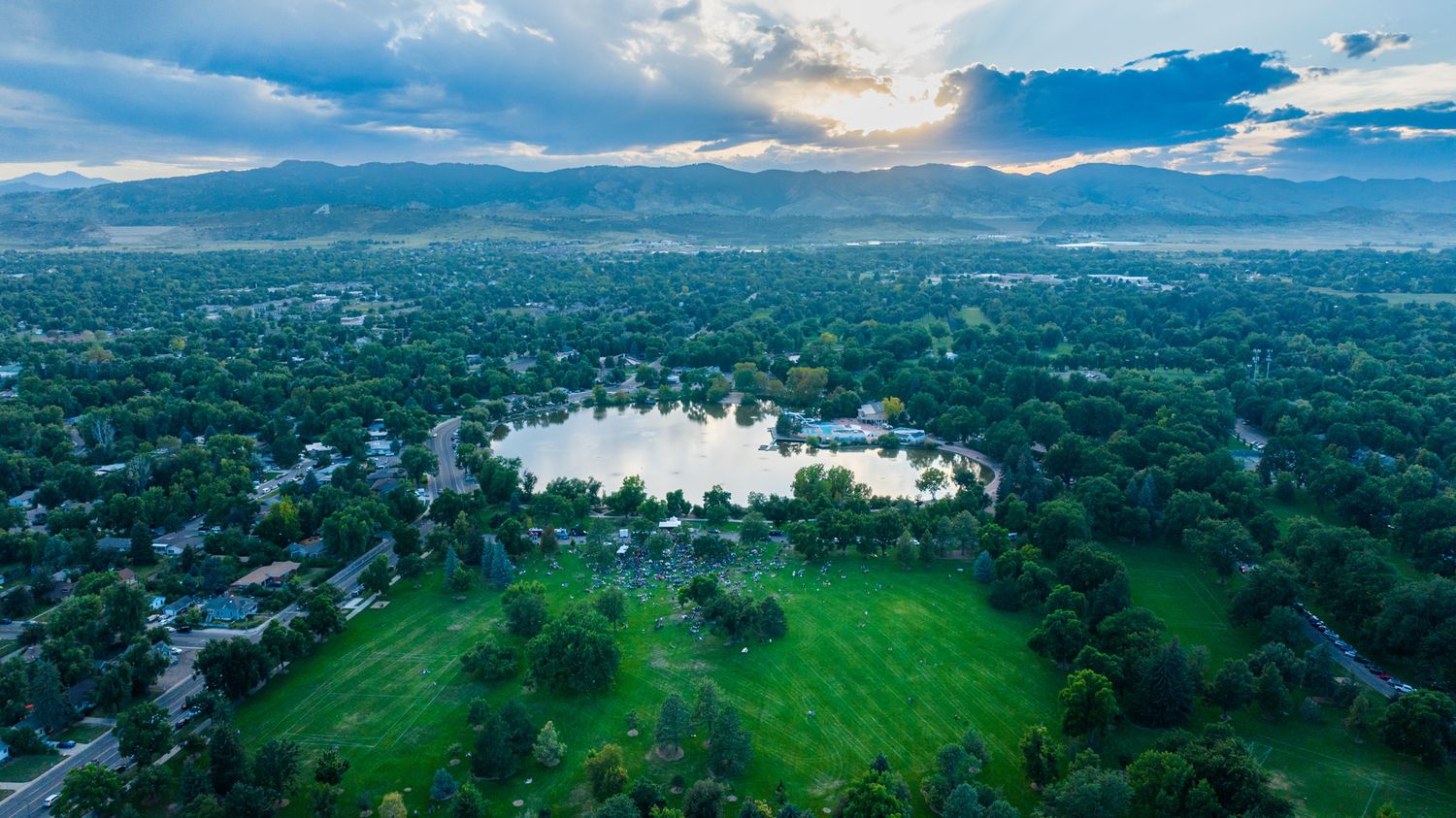 Aerial view of city park with lake surrounded by mountains and residential areas.