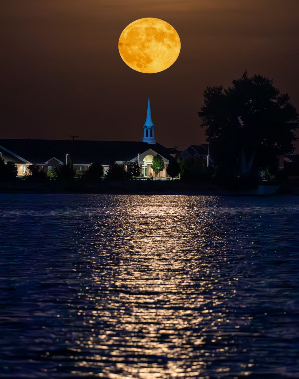 Full harvest moon reflecting golden light on dark water with church silhouettes.