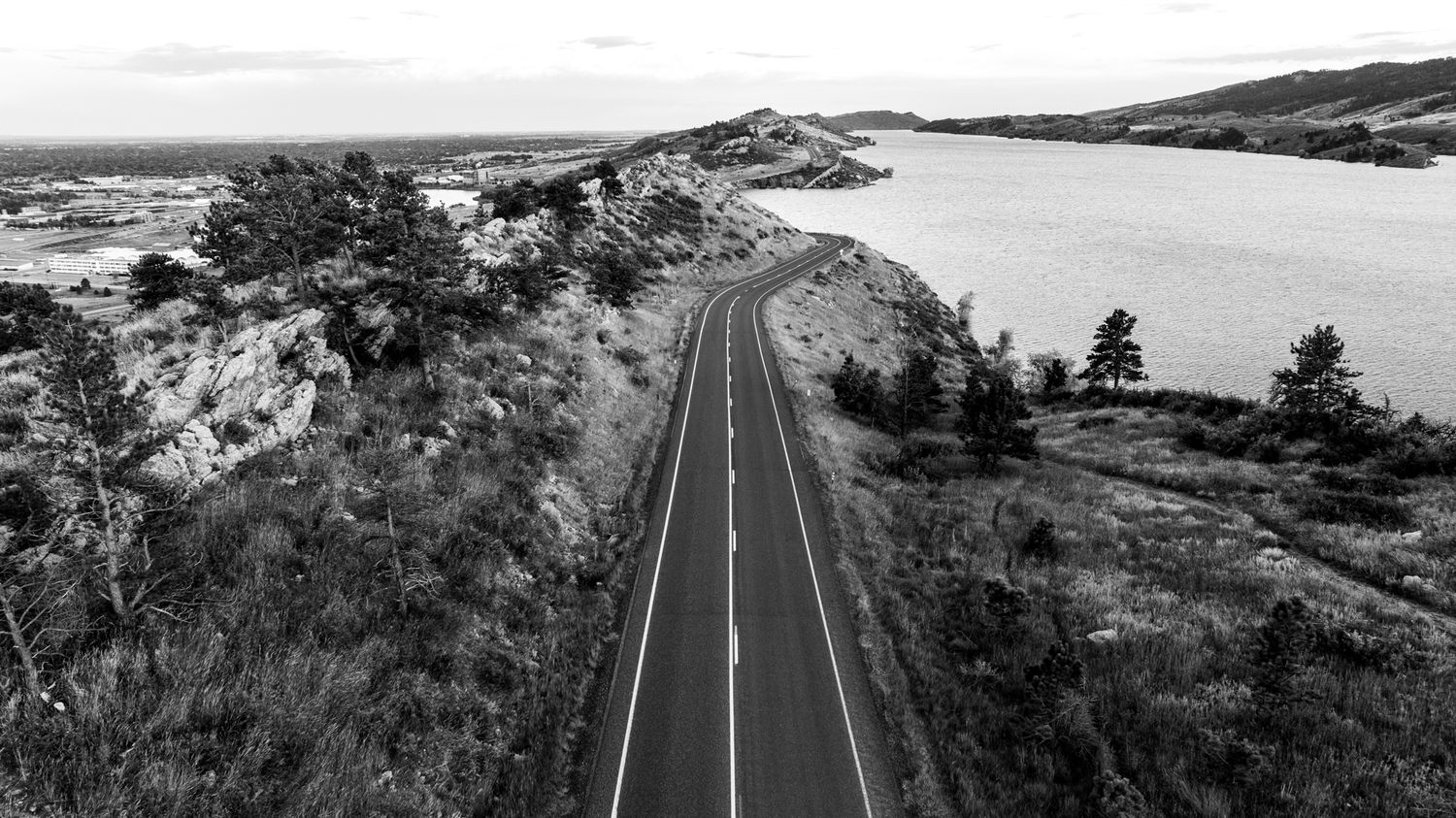Black and white panoramic view of a winding mountain road cutting through rugged terrain.