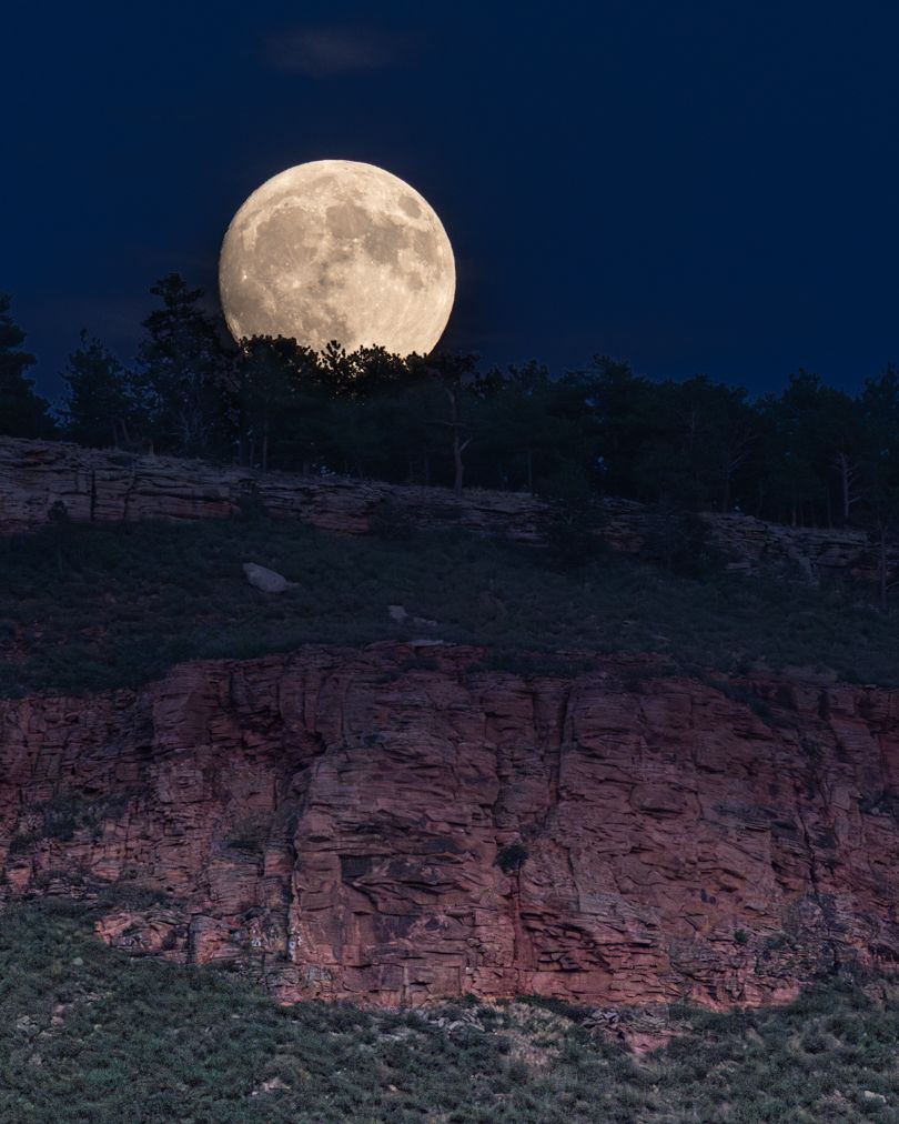 Full moon rising over red rock cliffs at dusk creates a dramatic desert landscape.