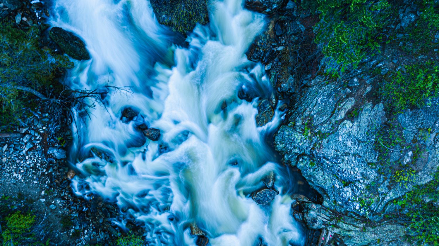 Rushing blue waterfall cascades over mossy rocks in a lush forest setting.