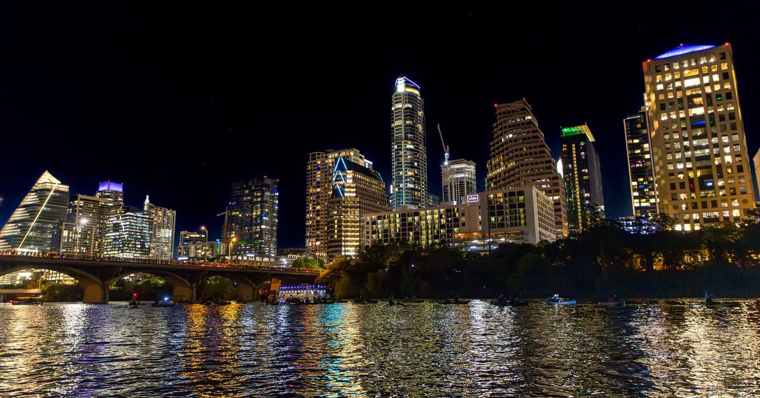 Austin skyline at night reflecting in Lady Bird Lake with illuminated skyscrapers.
