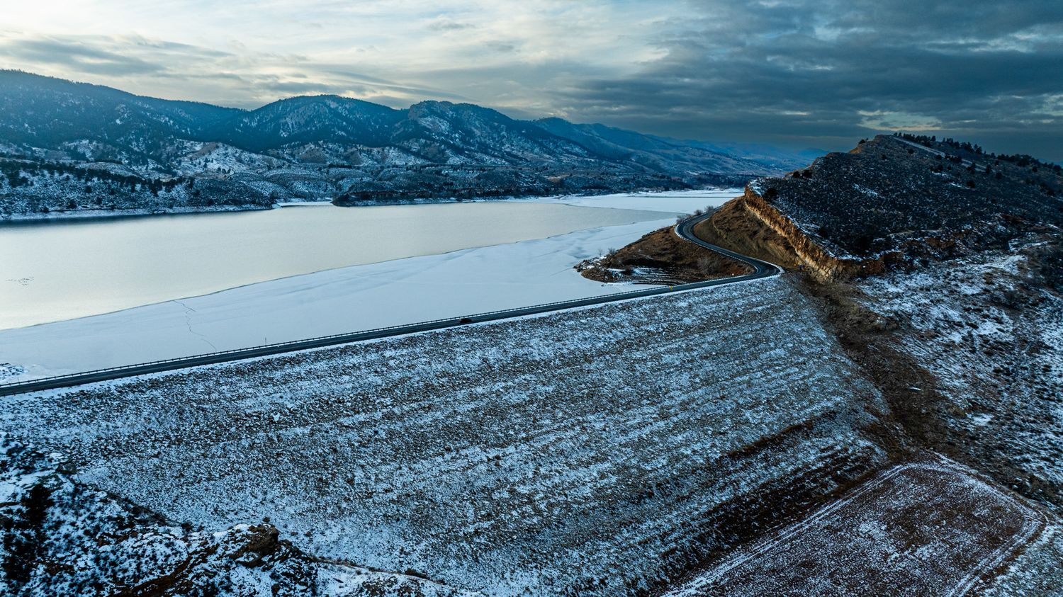 Snow-covered winter landscape with mountains and dramatic cloudy skies in panoramic view.