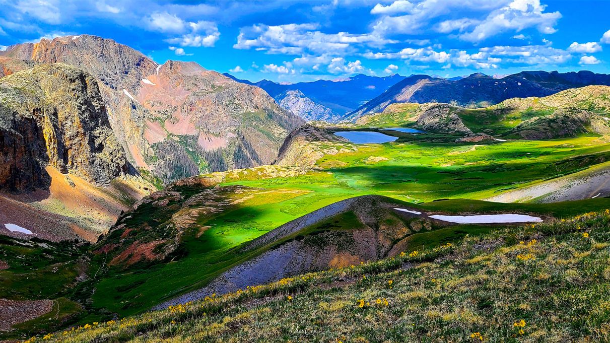 Rolling green hills and rugged mountain peaks create a stunning alpine landscape.