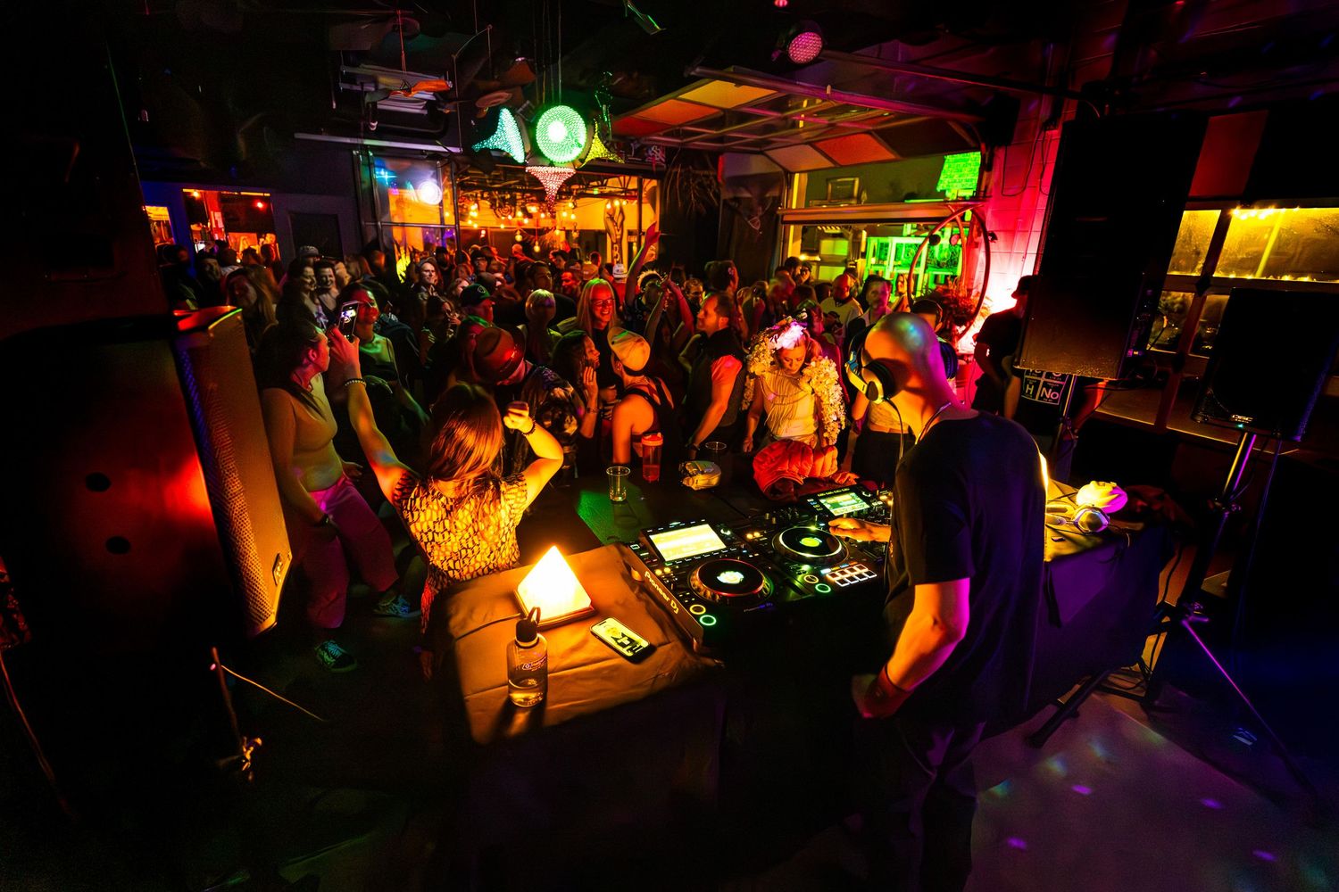 Crowded nightclub scene with colorful lighting and DJ equipment.