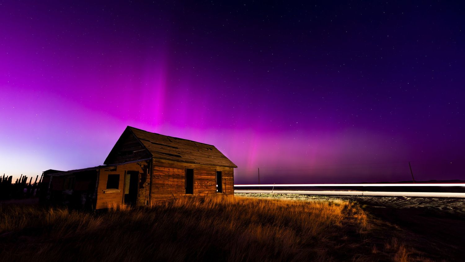 Purple and pink aurora borealis glowing over a rustic barn at night.