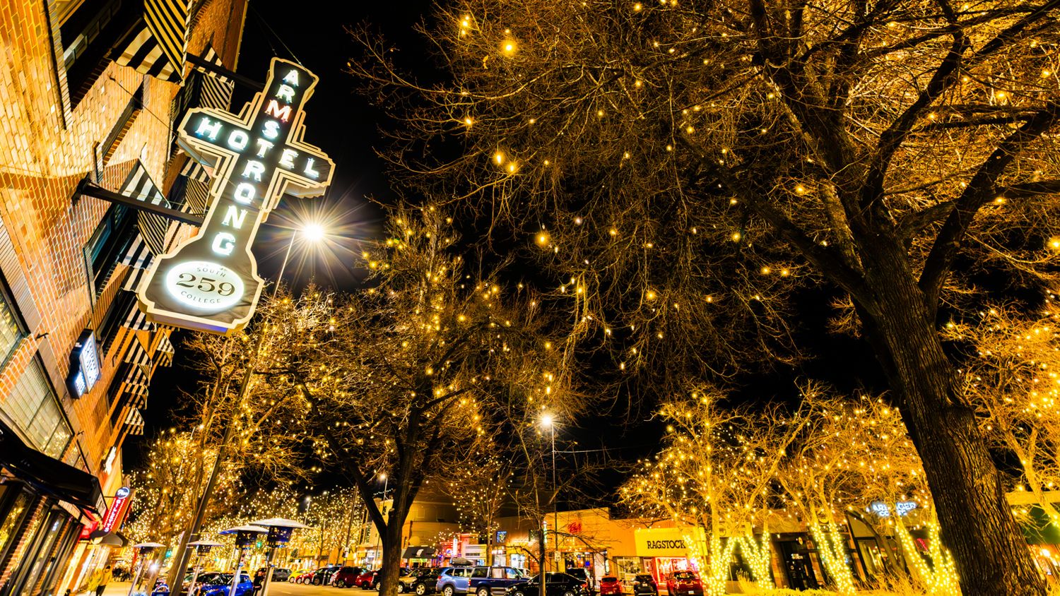Nighttime street scene with illuminated holiday lights and crosses glowing in tree branches. The Armstrong Hotel in Fort Collins, Colorado.