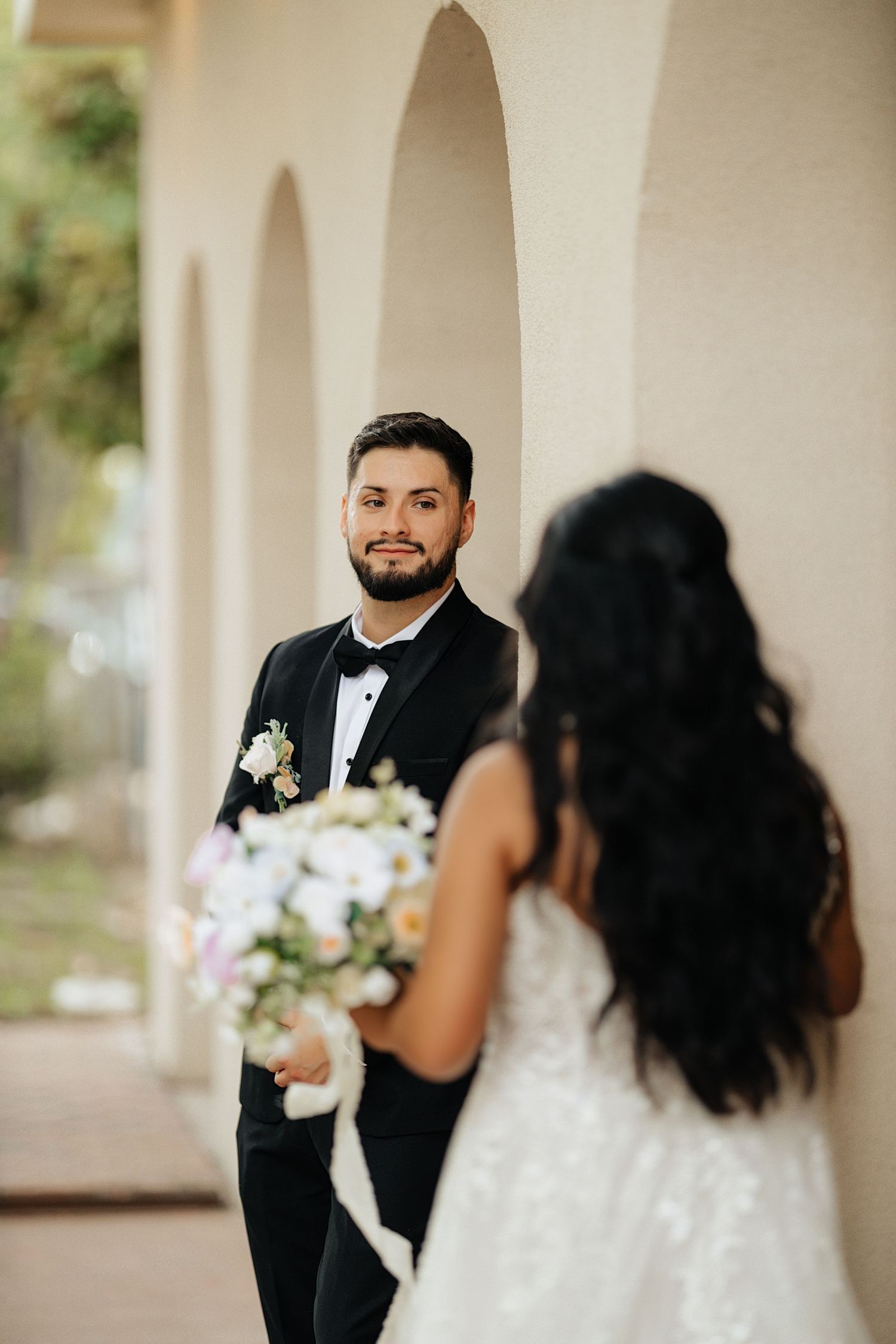 A bride and groom share their first look moment during an outdoor wedding ceremony under white arches.