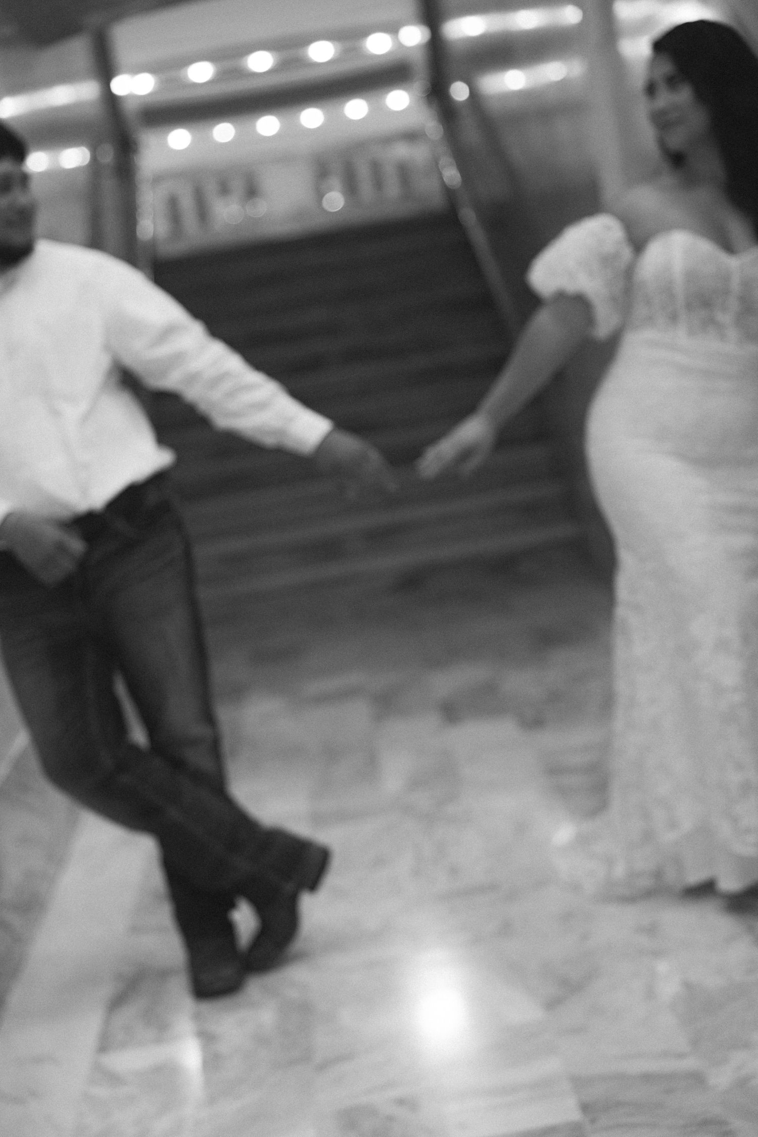 Black and white image of a bride and groom reaching for each other's hands.