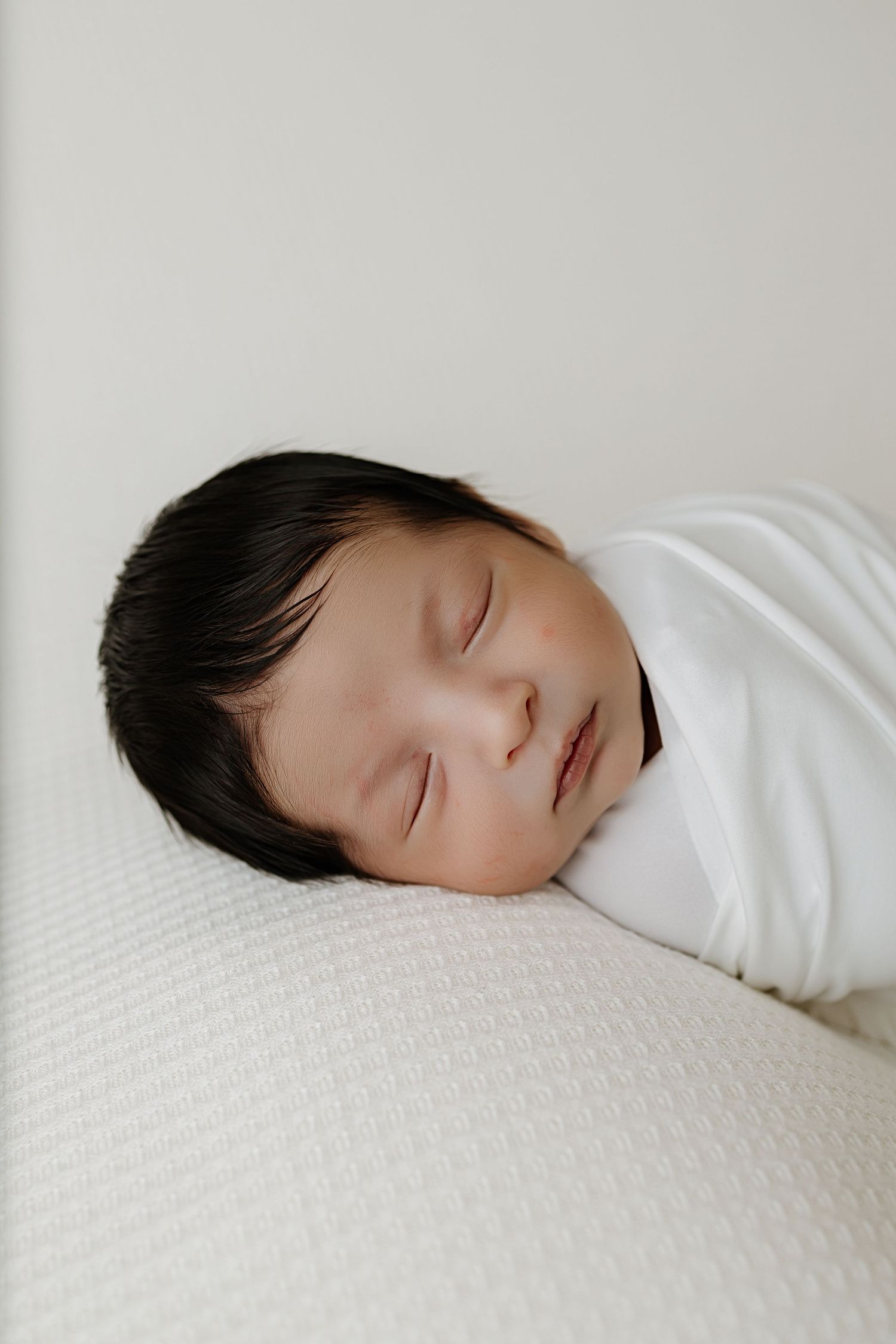 Newborn wrapped in a white blanket and posing during his newborn photo session.