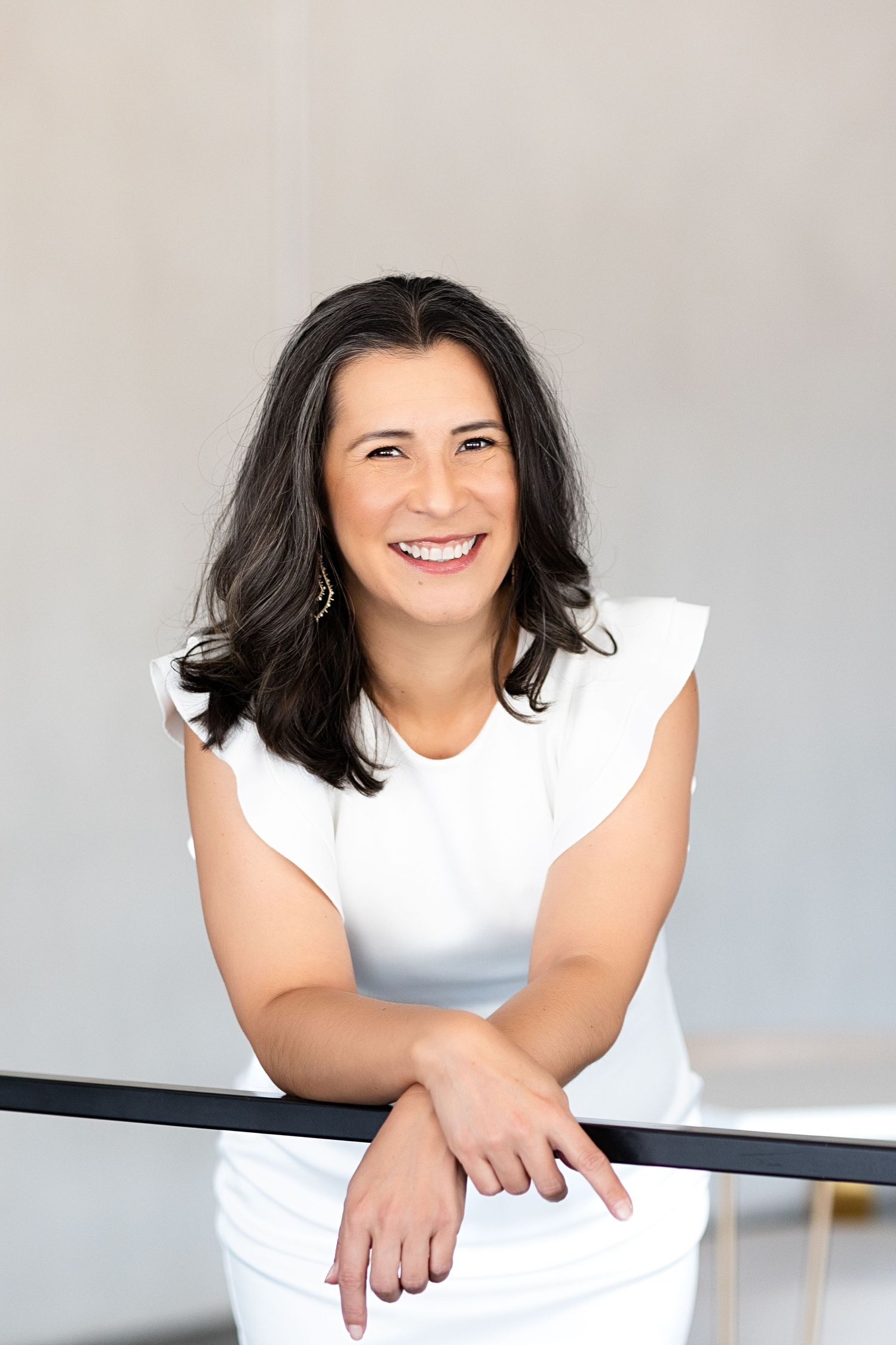 Woman in a white dress posing on a railing during a headshot session.