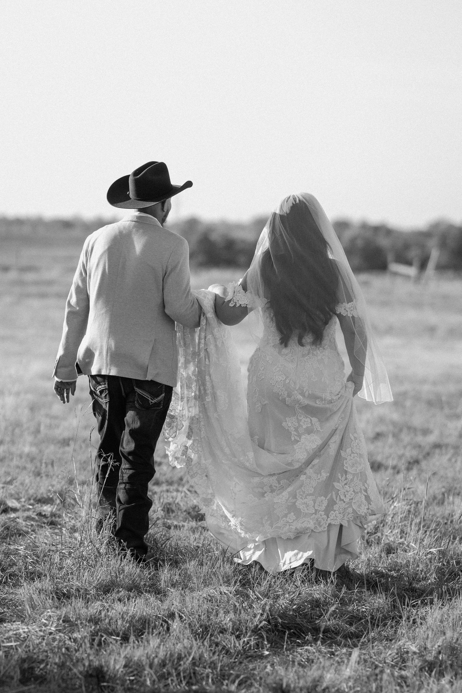 Bride and groom holding hands. Western bride and groom. Western wedding day with a hat and a long wedding veil.