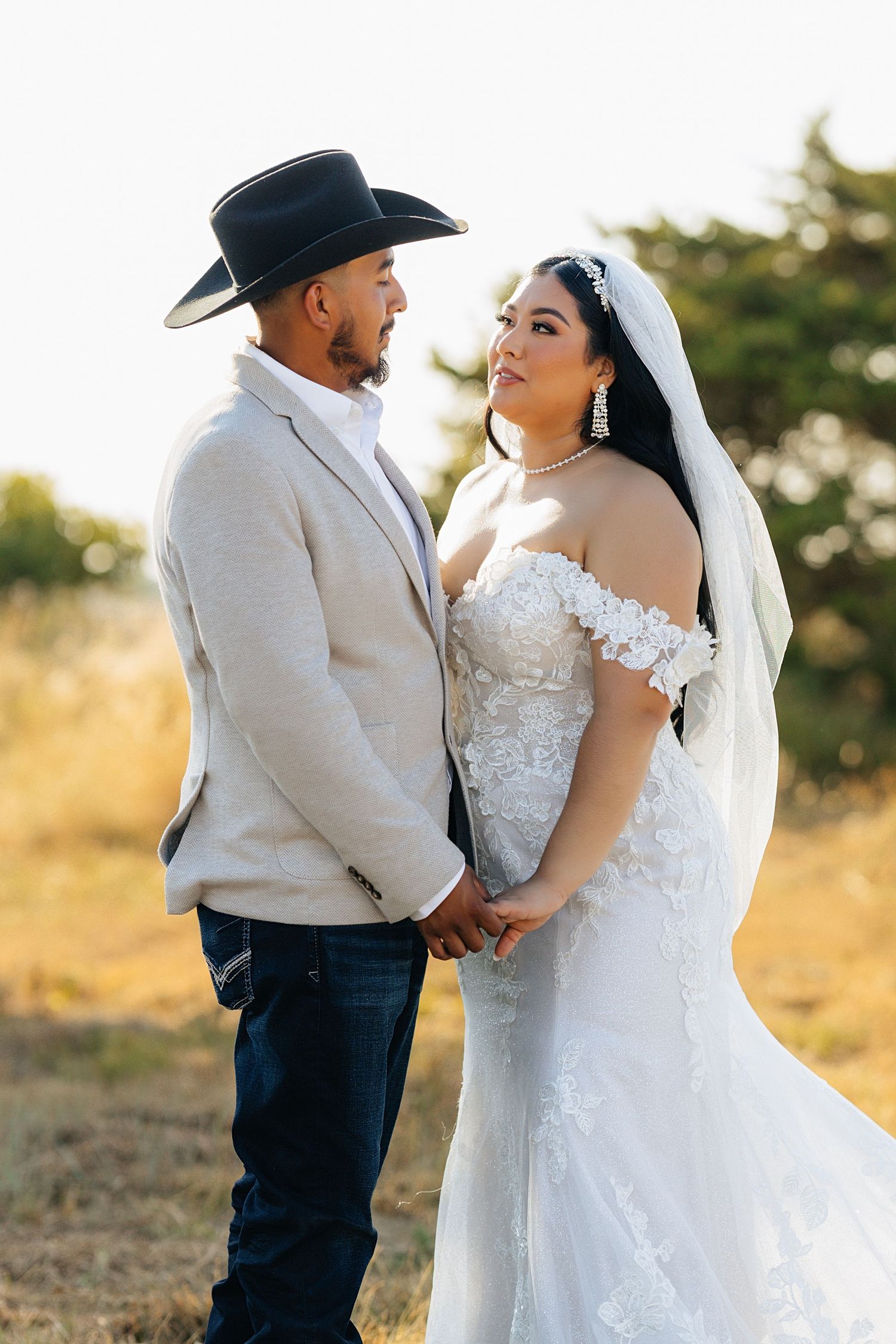 Bride and groom holding hands. Western bride and groom. Western wedding day with a hat and a long wedding veil.