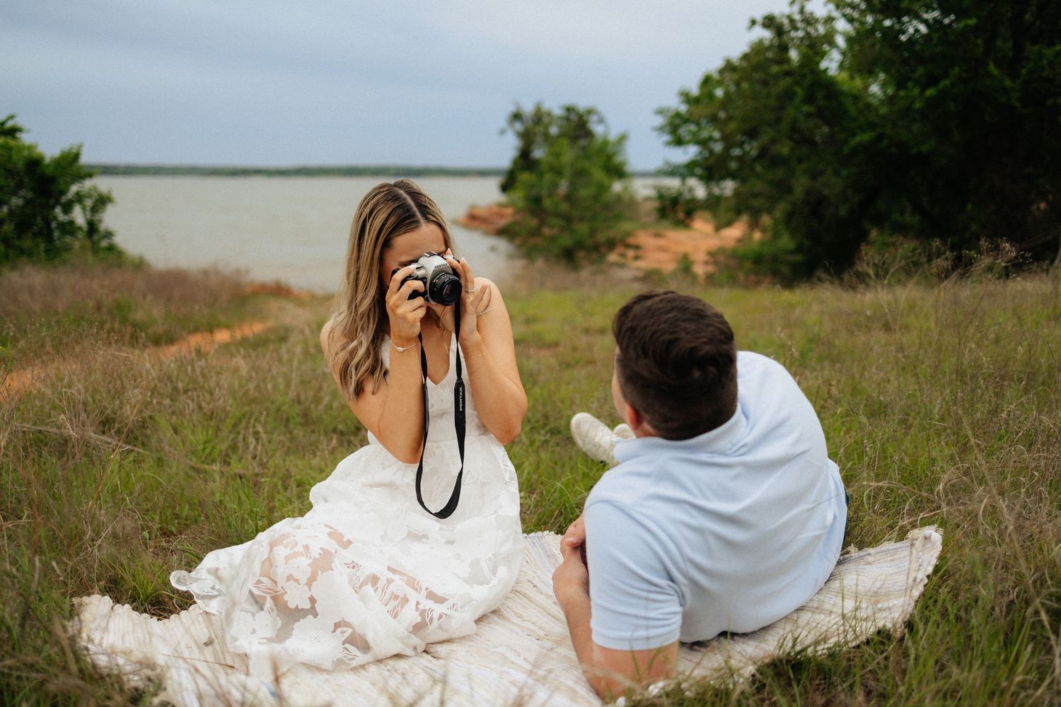Engagement session by the lake during golden hour. Bride is wearing a white dress. Lake arcadia engagement session. Groom is wearing blue.