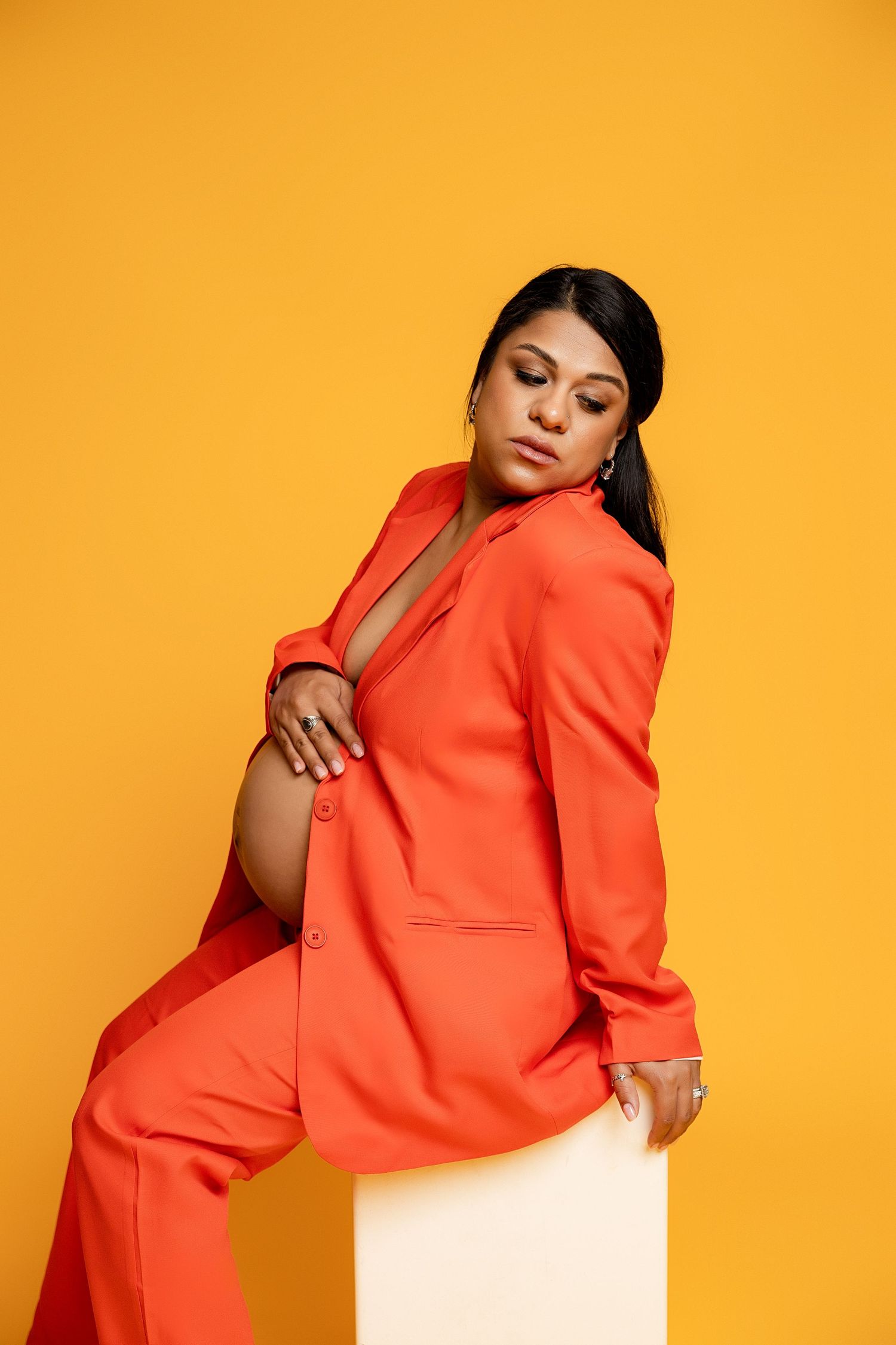 Maternity session of a woman in an orange suit with a yellow background. Hispanic woman during a maternity session.
