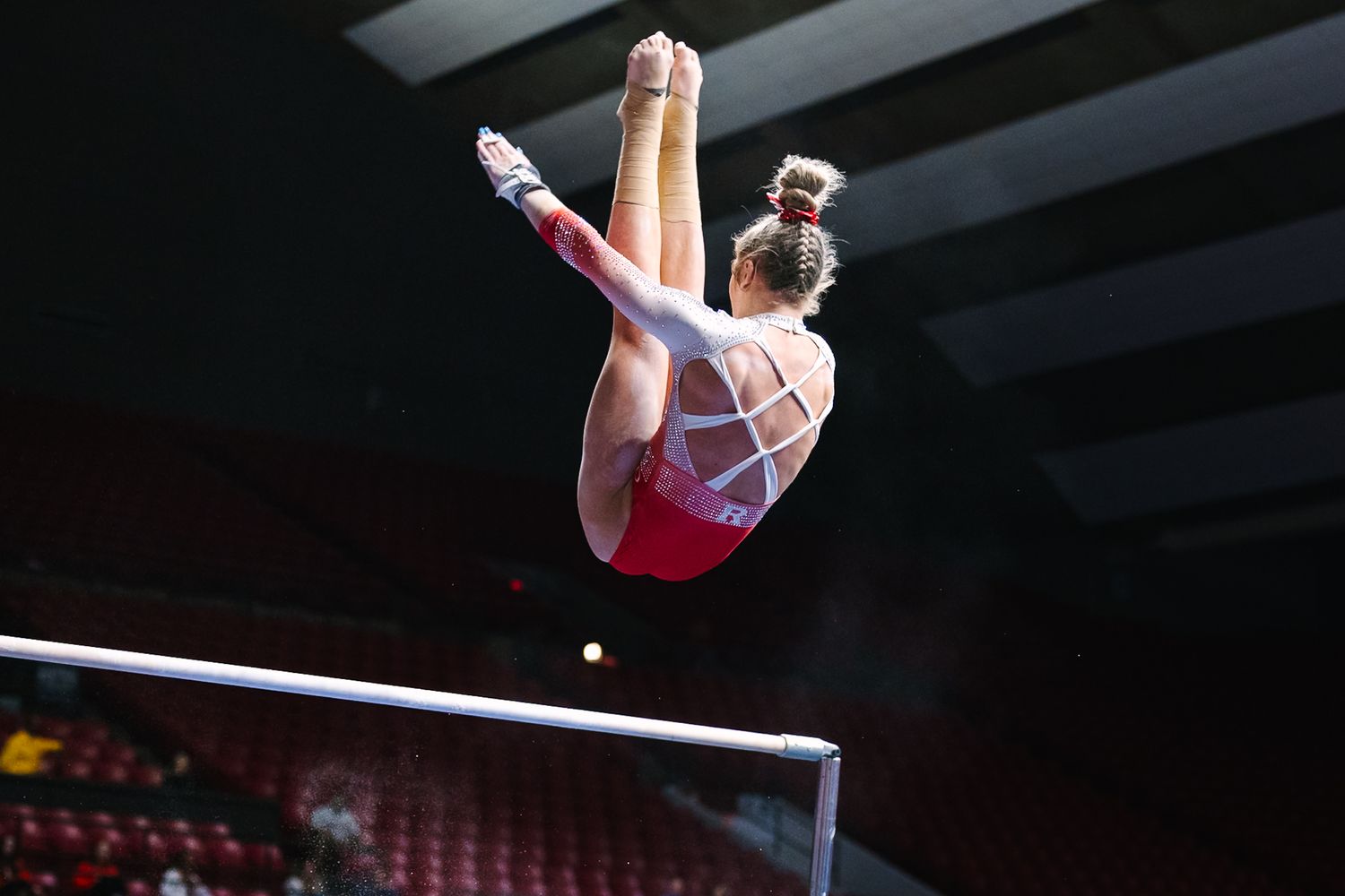 Gymnast performing a handstand on high bar during artistic gymnastics competition at indoor arena.