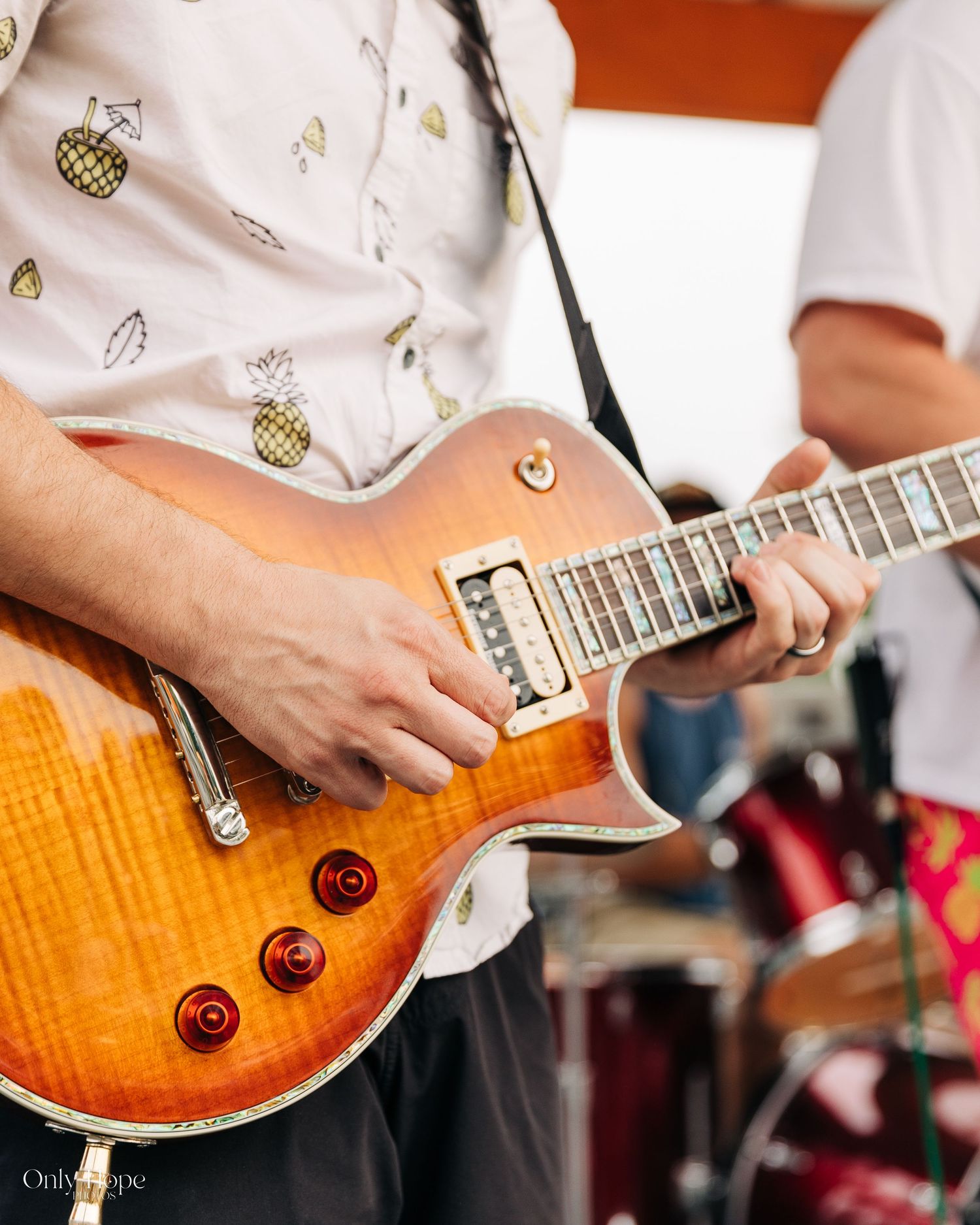 Close-up view of hands playing an orange flame maple Gibson Les Paul guitar during a live performance.
