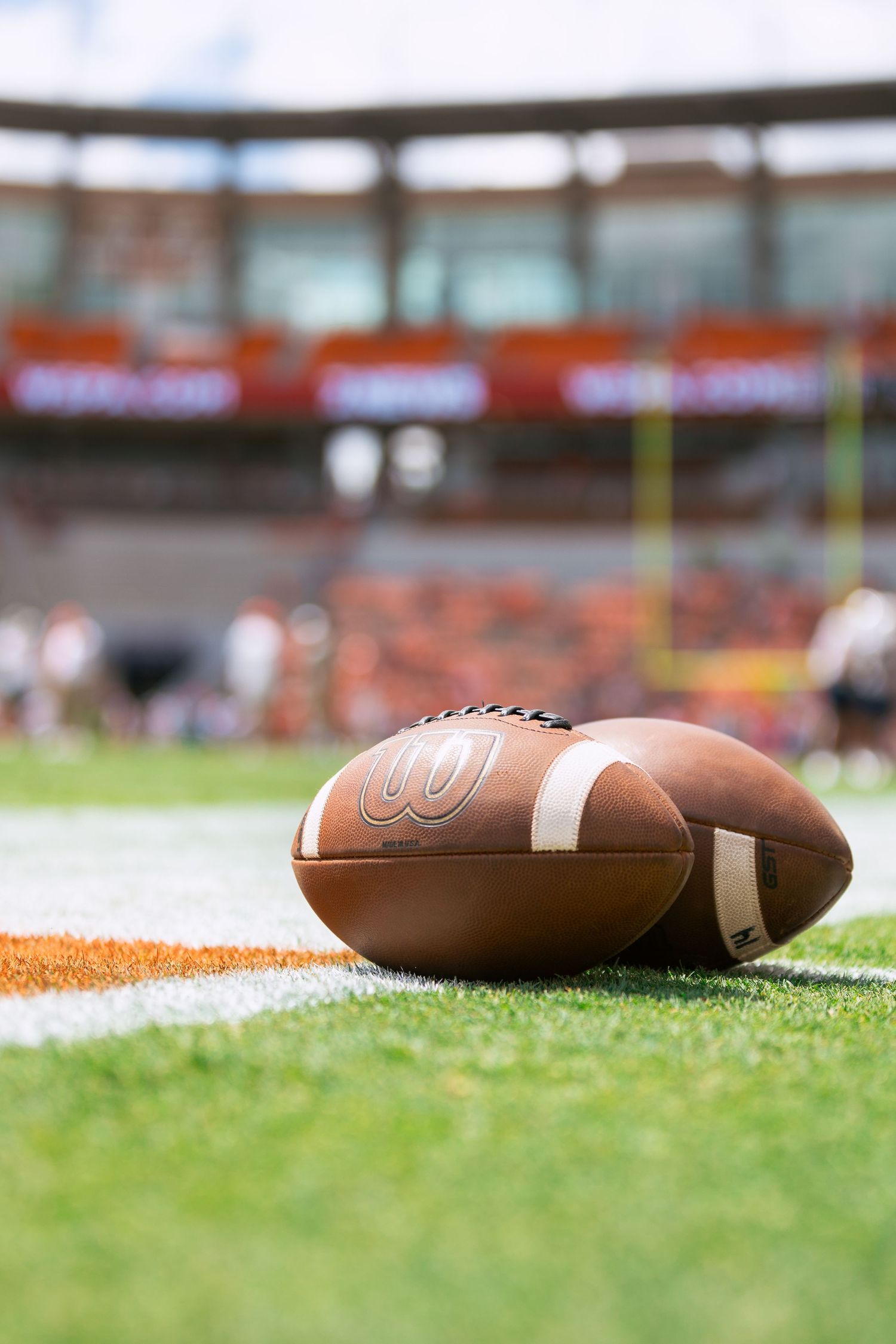 Close up of football resting on turf field with stadium in background.