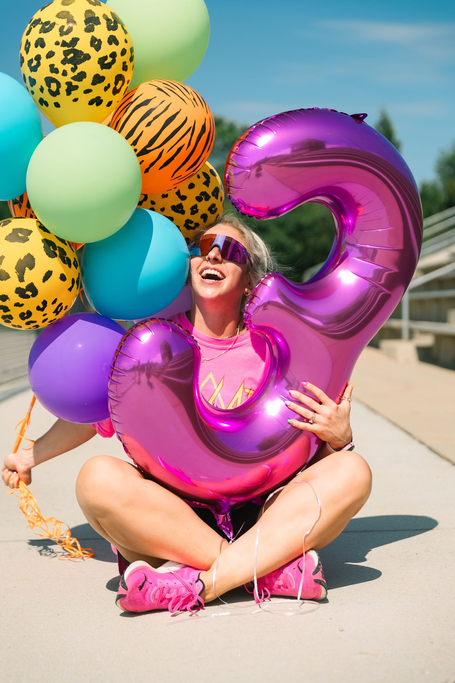 Colorful celebration scene with animal print and solid balloons alongside a large pink metallic number 5 balloon outdoors.