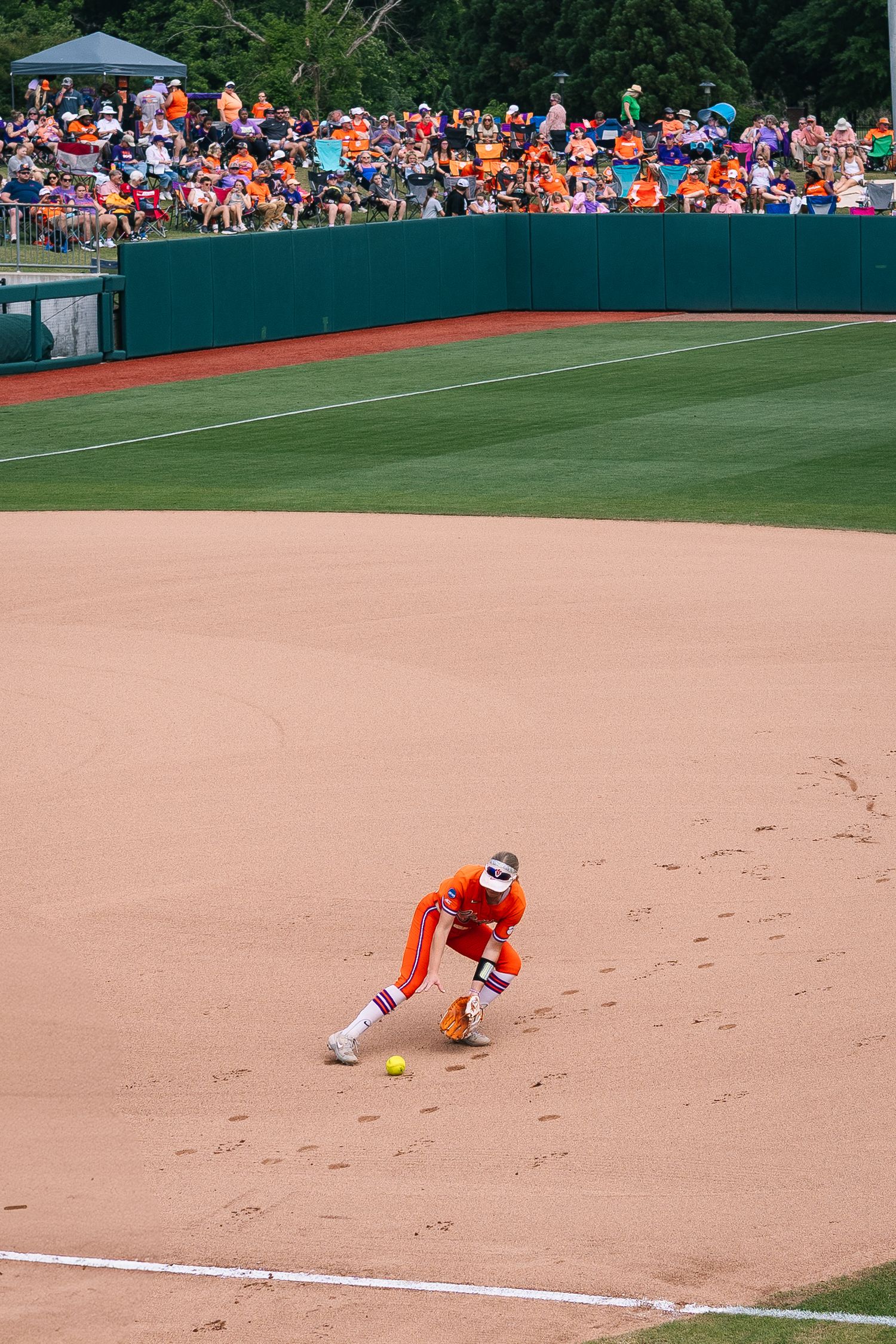 Baseball player in orange uniform crouches on the infield dirt while crowd watches from green outfield wall seats.