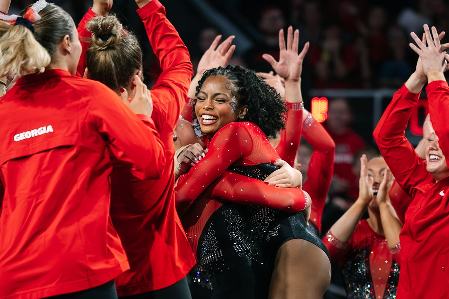 Georgia Bulldogs gymnastics team celebrating together in red leotards, sharing hugs and high-fives during a meet.
