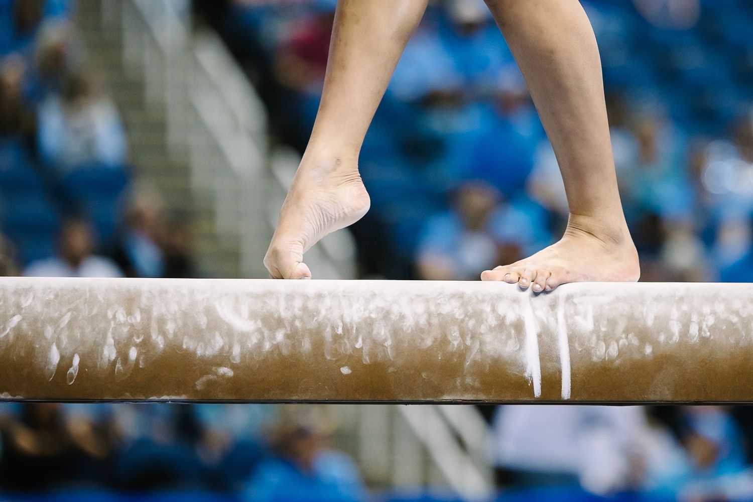 Close-up of gymnast's feet gripping a balance beam during competition performance with chalk visible.
