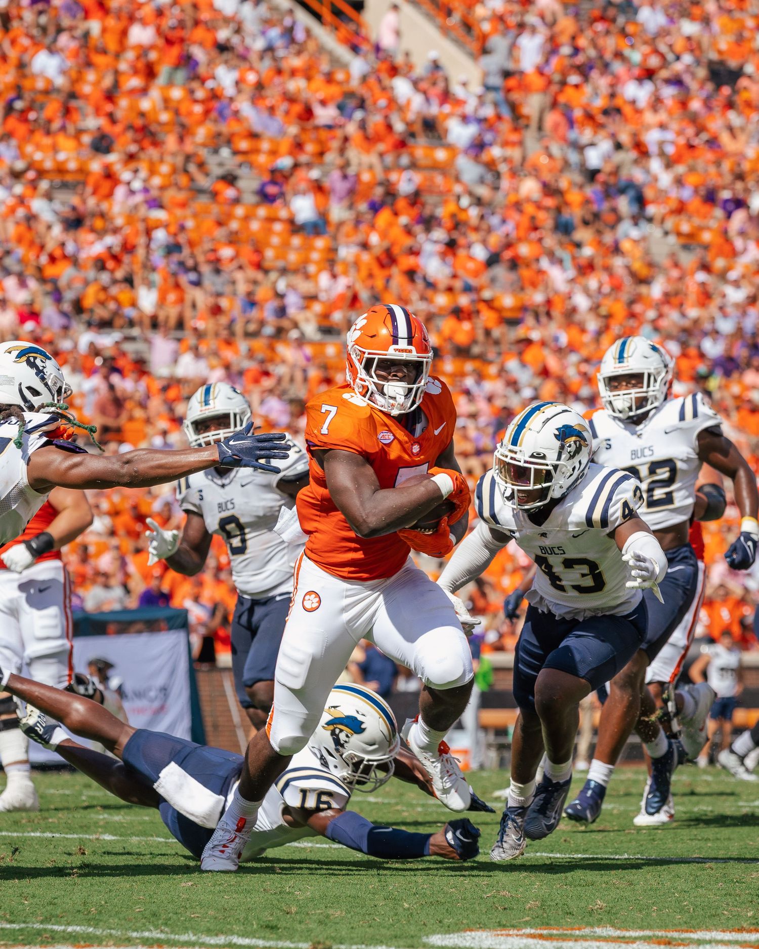 Football players from opposing teams collide during an intense goal-line play at a packed college stadium with orange crowd.