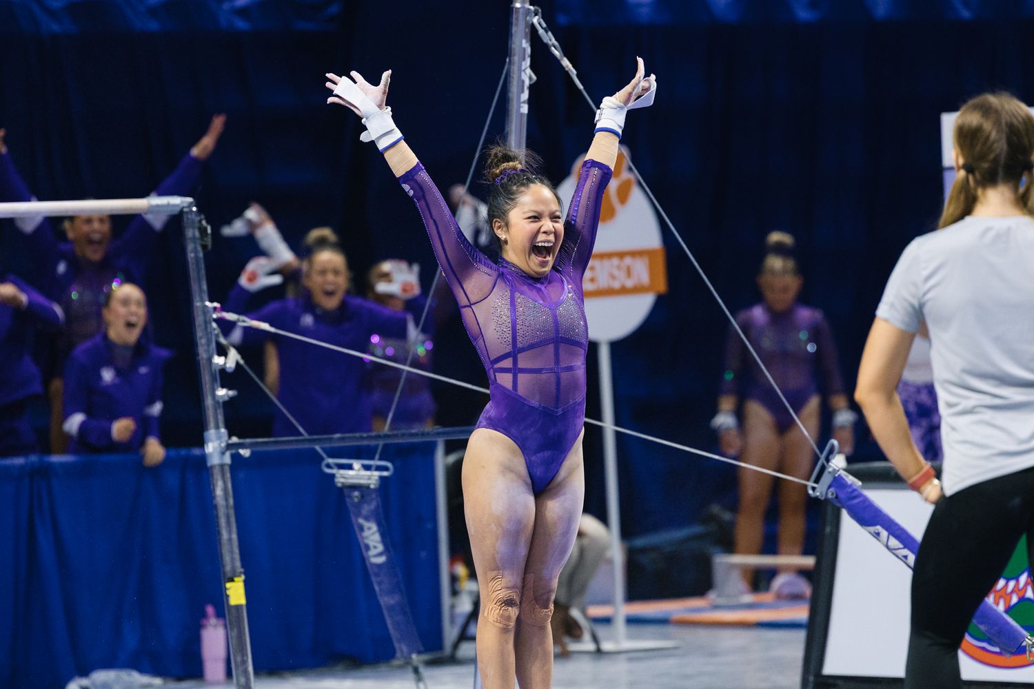 Gymnast in purple leotard celebrates with raised arms during college competition at Florida Gators meet.