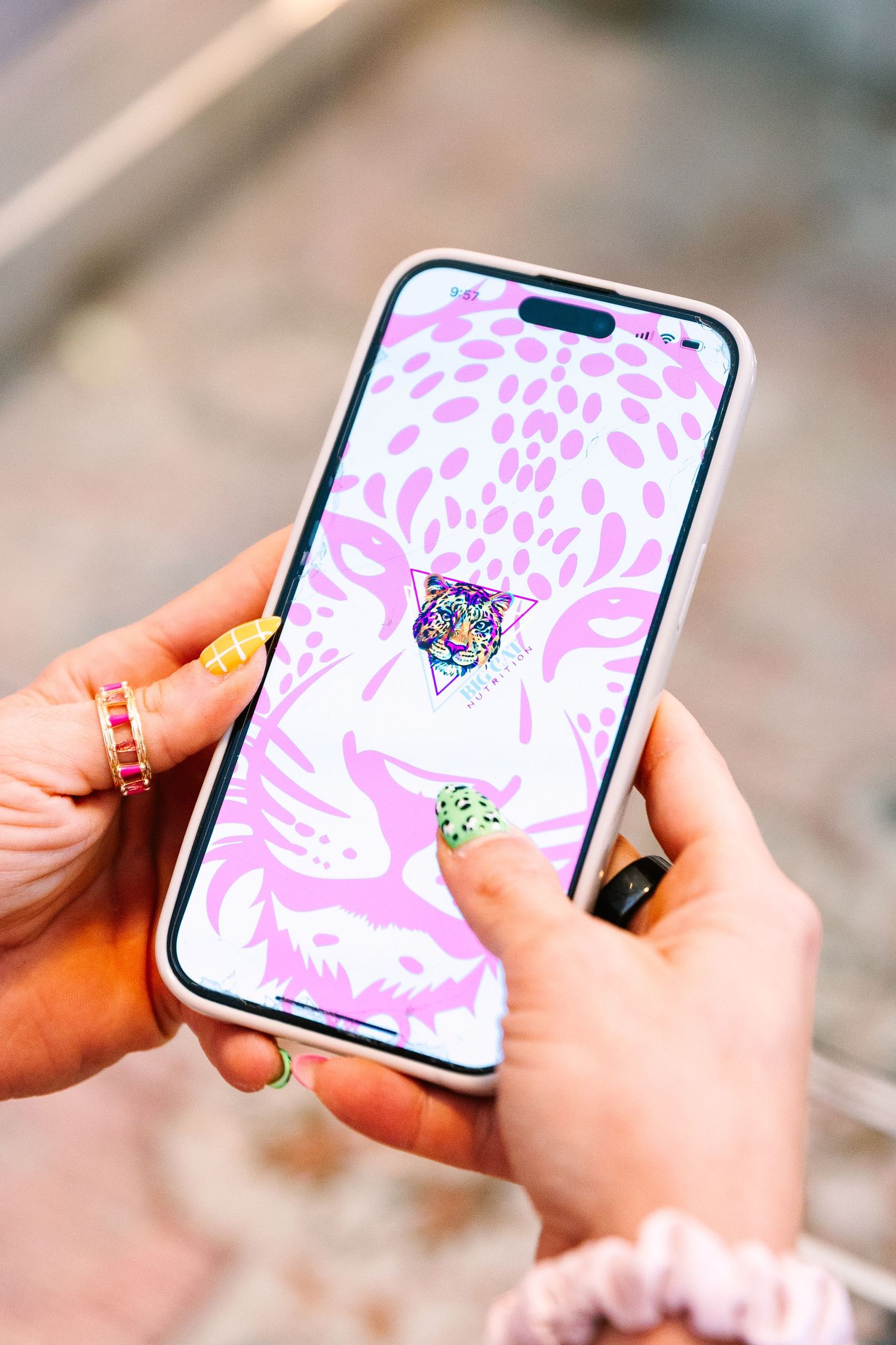 Hands with manicured nails holding an iPhone displaying a pink floral pattern and colorful geometric design on the screen.