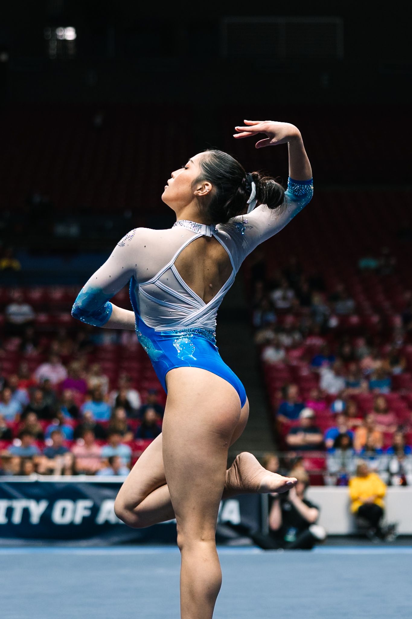 Gymnast performing an artistic floor routine in a white and blue leotard at a competition.