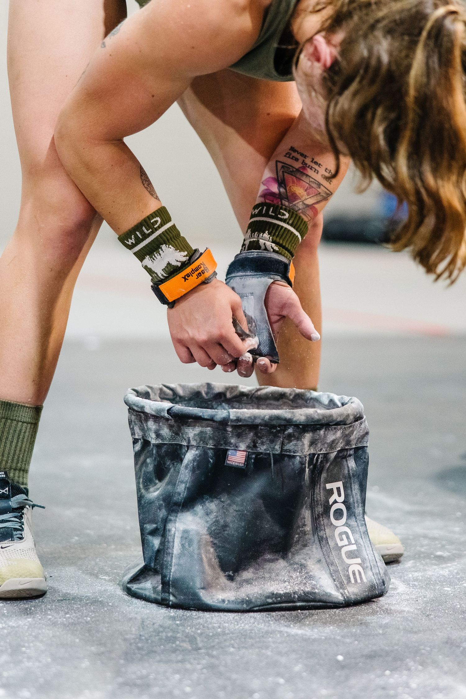Close-up shot of chalk-covered hands reaching into a climbing chalk bag with orange and black wrist accessories.