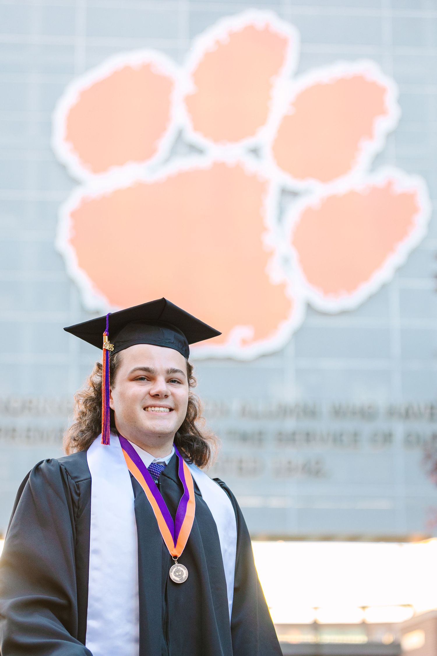 Graduate posing in cap and gown with Clemson University paw logo in the background.