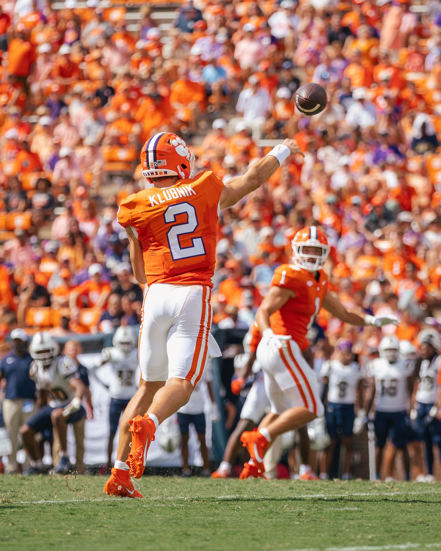 Football player in orange jersey kicks field goal during game with crowd in background.