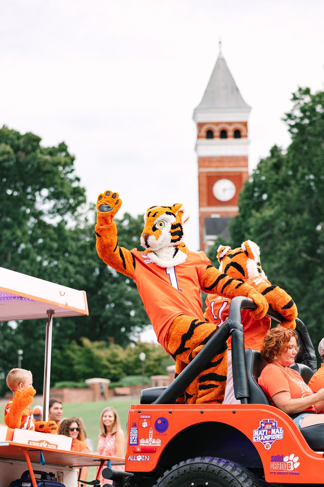 Clemson University mascot poses enthusiastically in front of iconic Tillman Hall clock tower during a campus event.