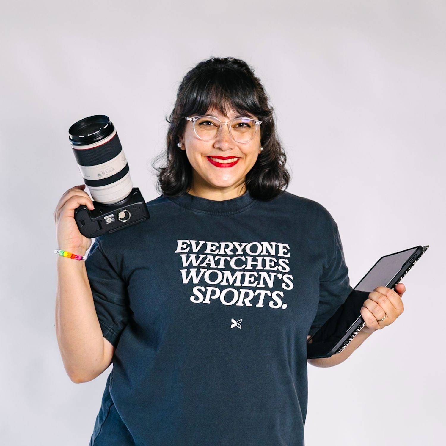 Person in black t-shirt showcasing photography equipment with multiple camera lenses and gear.