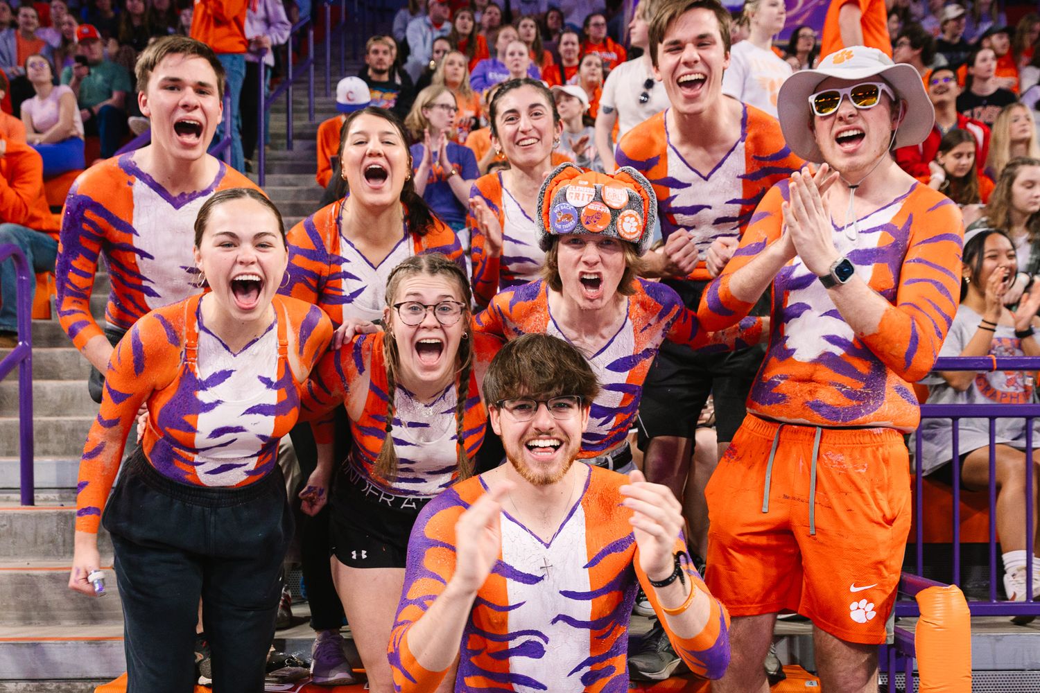 Enthusiastic college fans in orange and white striped uniforms celebrate during a sporting event.