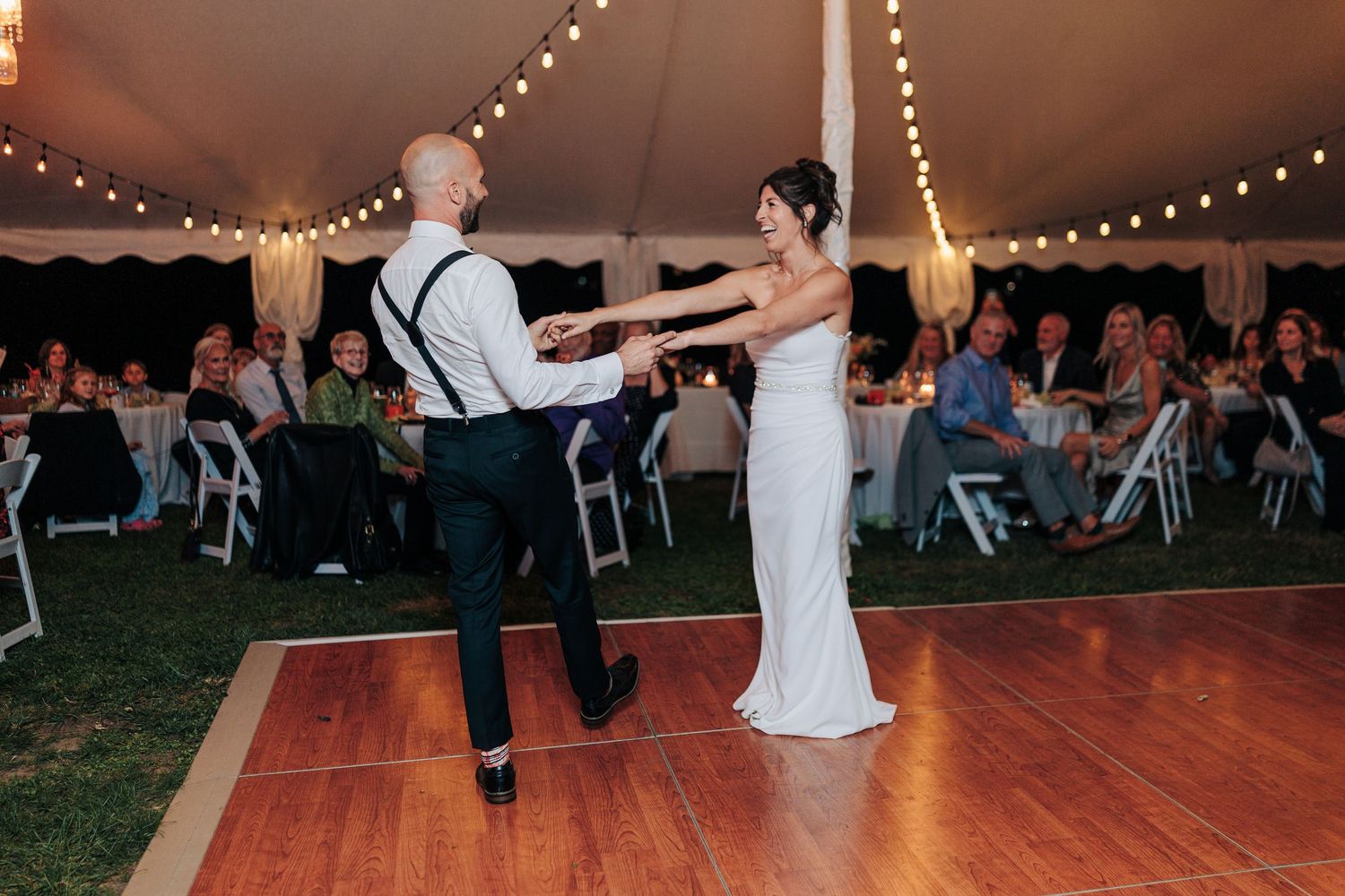 Wedding reception dance floor under tent with string lights and guests dancing.