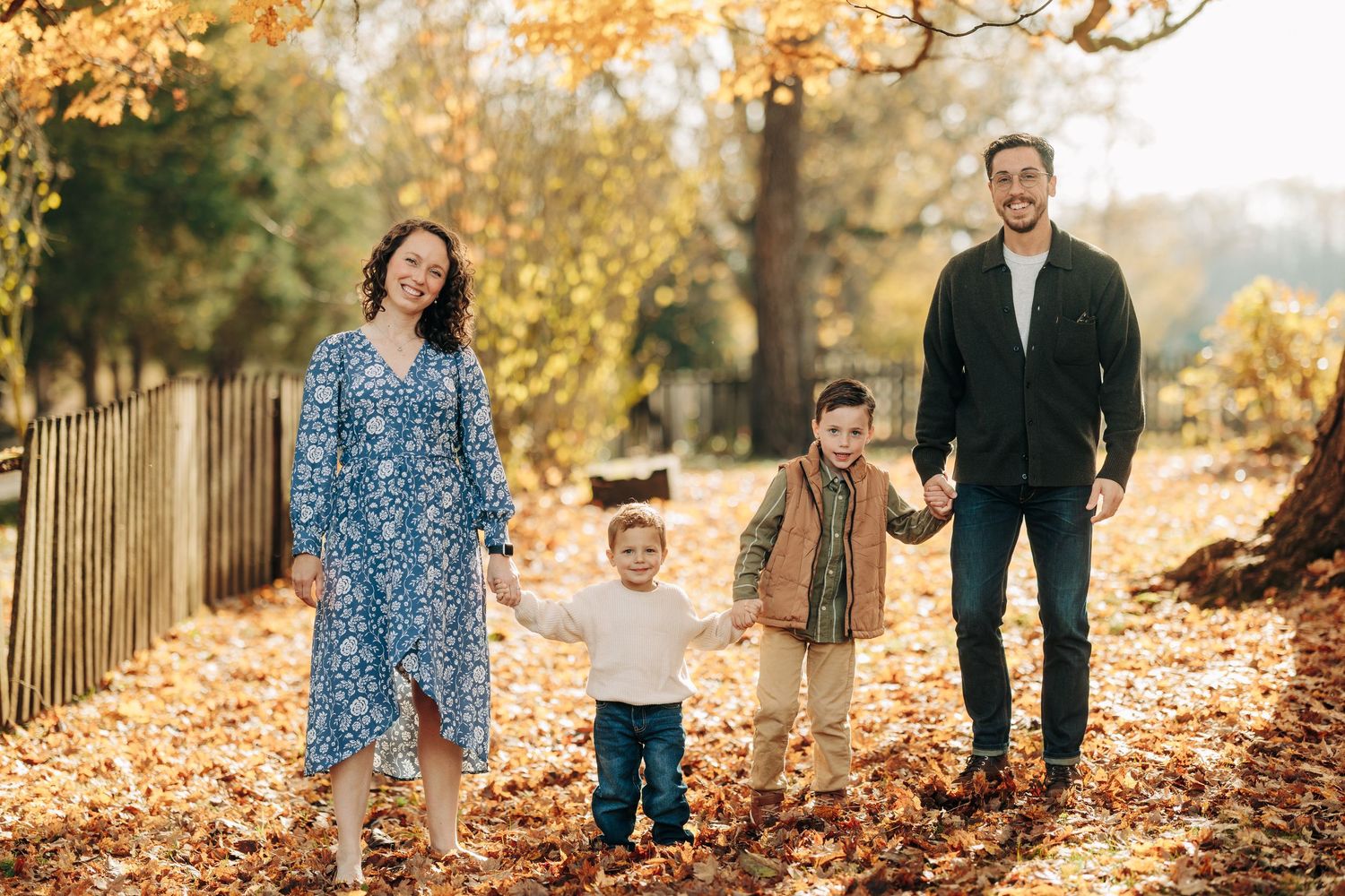 Family enjoying a warm autumn day together in a park with golden fallen leaves and sunlight filtering through trees.