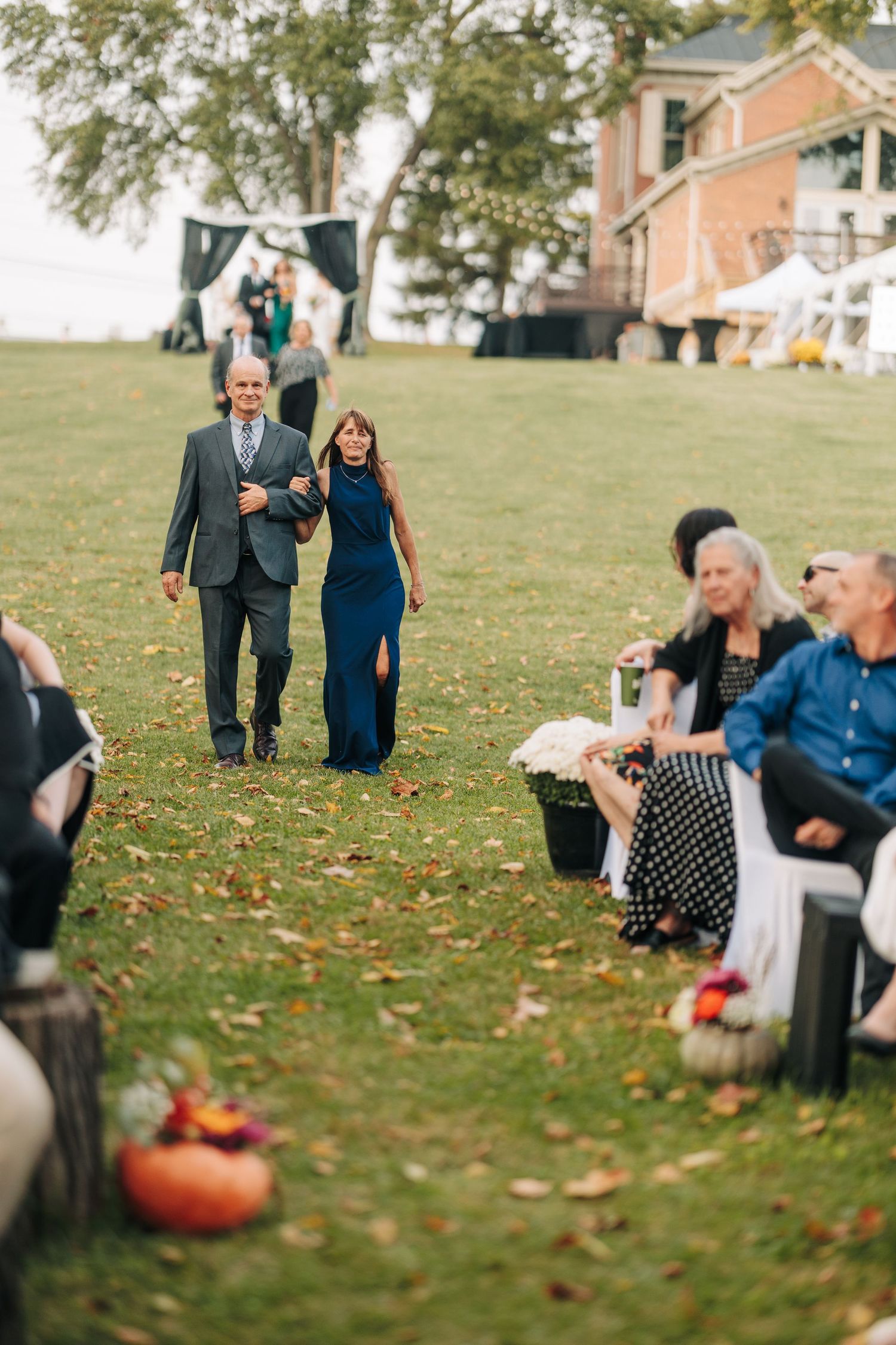 A group of guests sitting on grass during an outdoor autumn wedding with scattered leaves and pumpkins.