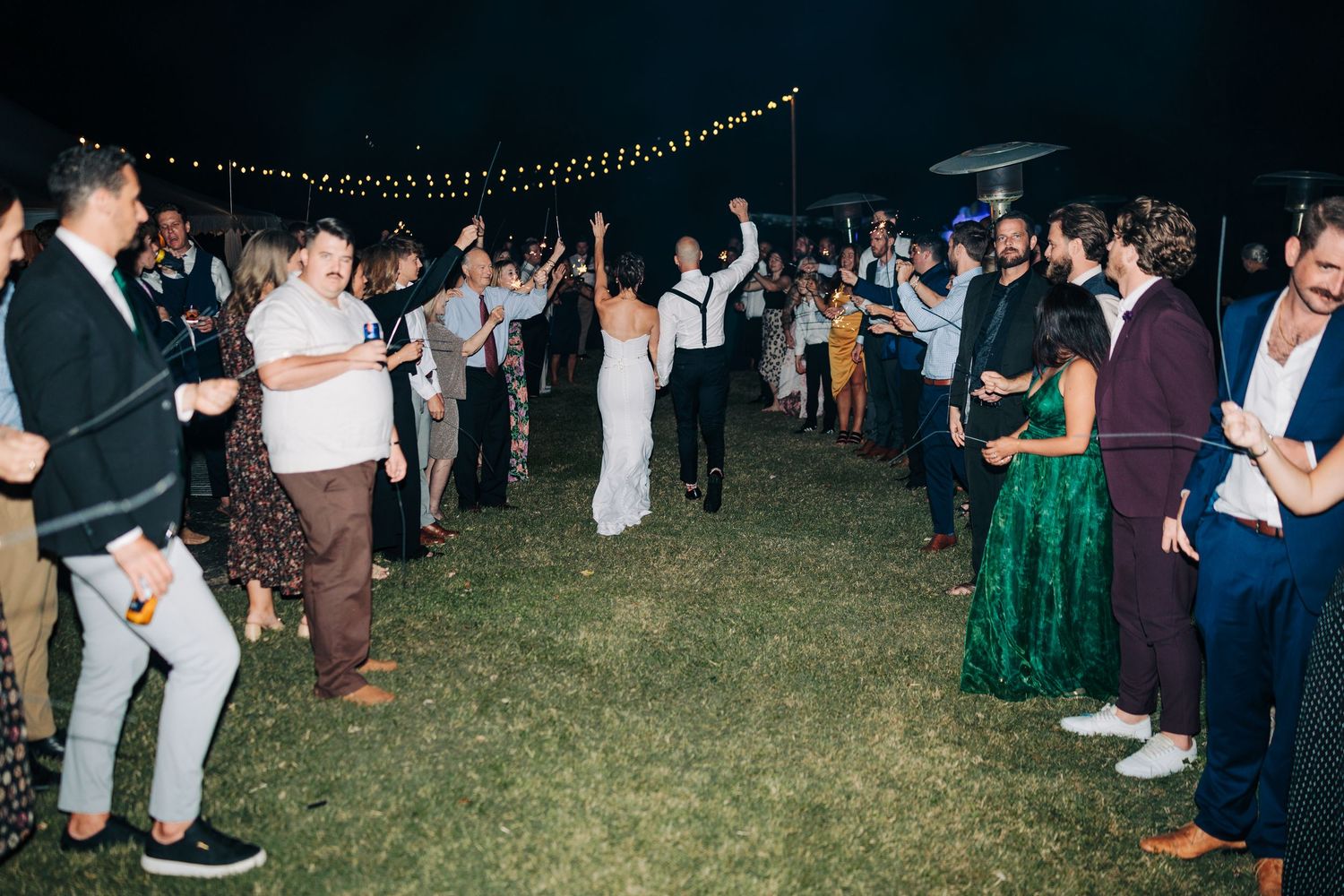 Wedding reception guests dancing under string lights at outdoor evening celebration.